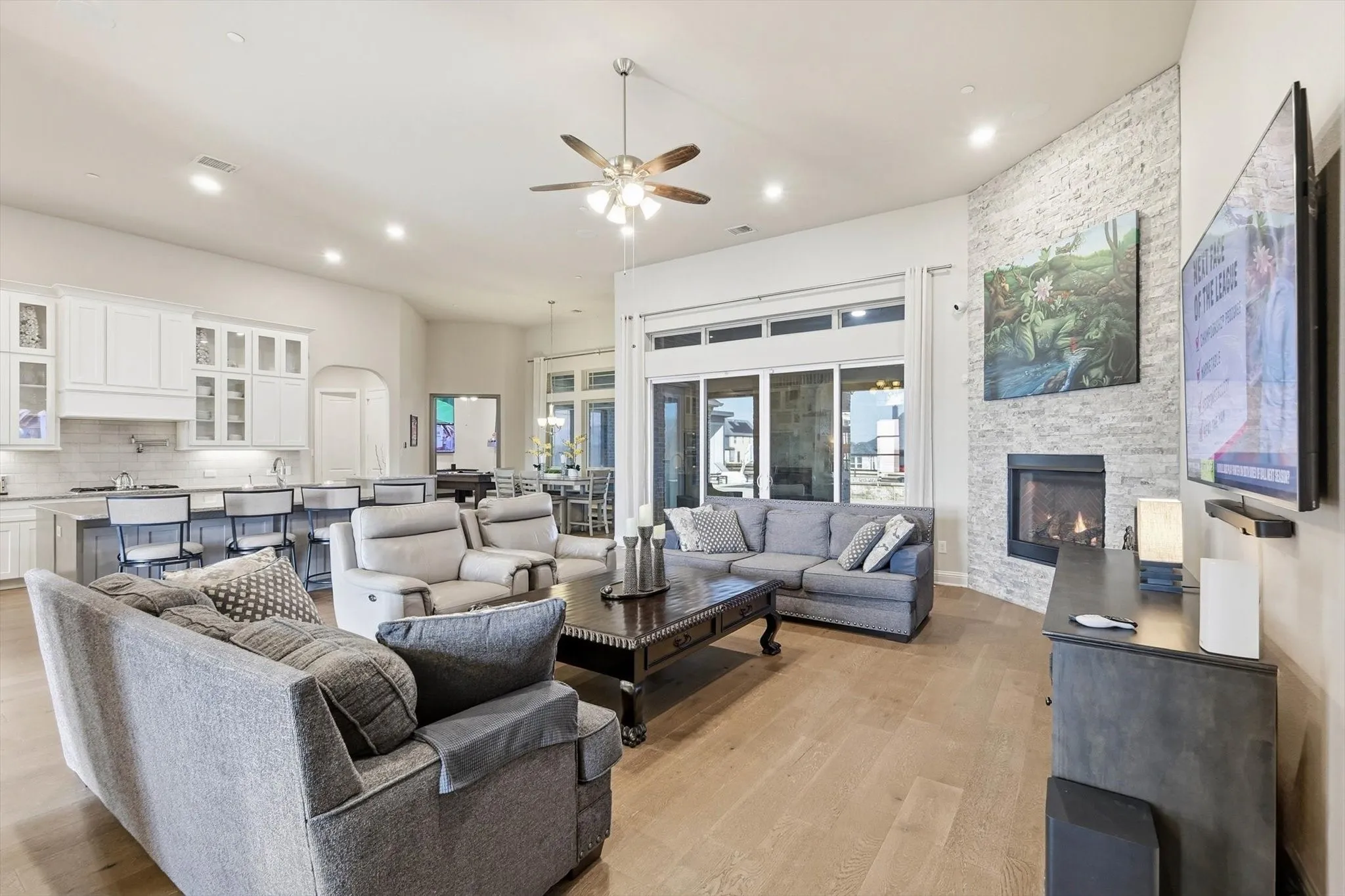 Spacious open-concept living area featuring light wood-finish flooring, a stone accent wall with a built-in fireplace, and expansive sliding glass doors
