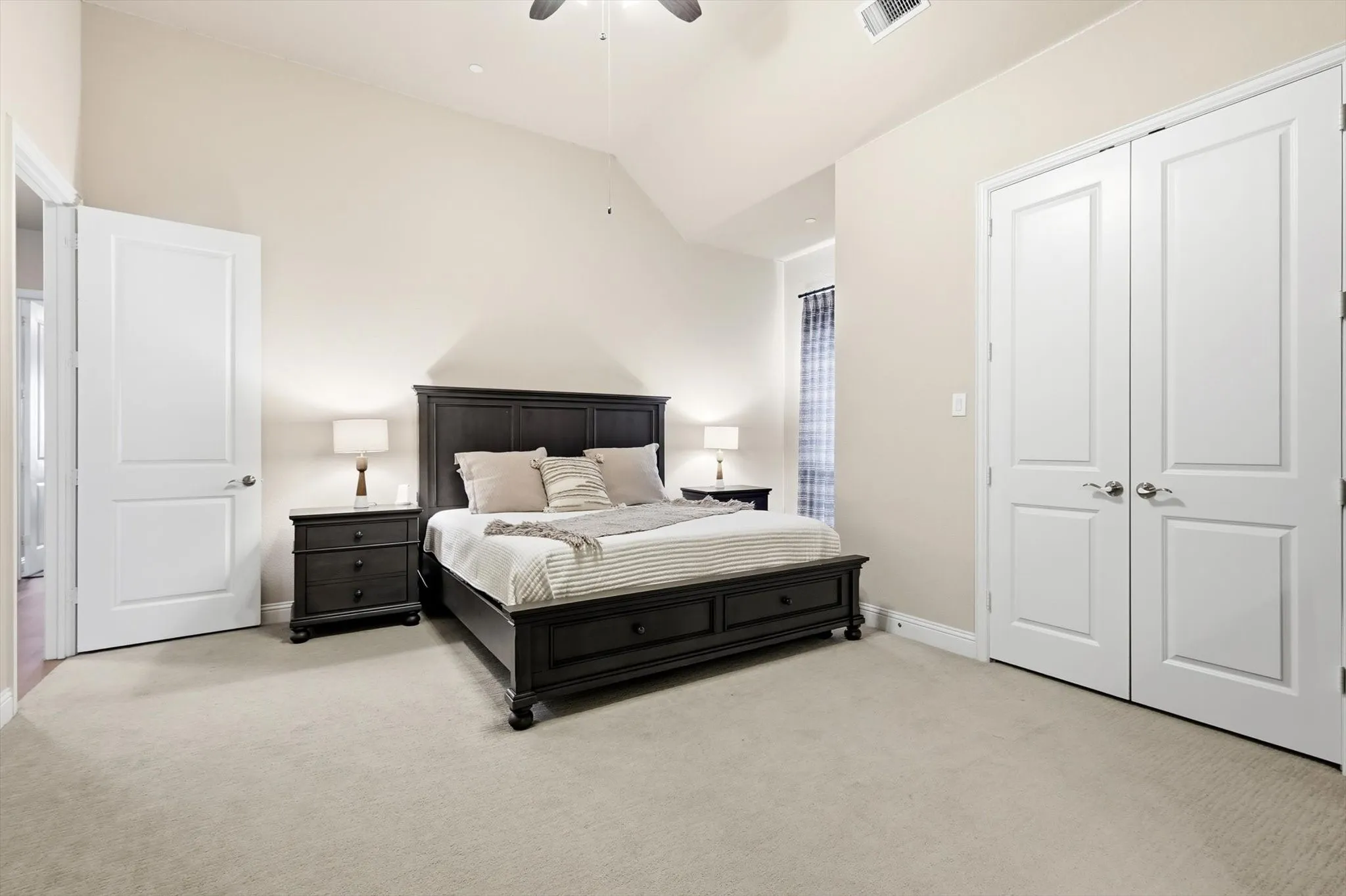 Spacious bedroom featuring vaulted ceilings, light neutral wall paint, and light-toned carpeting