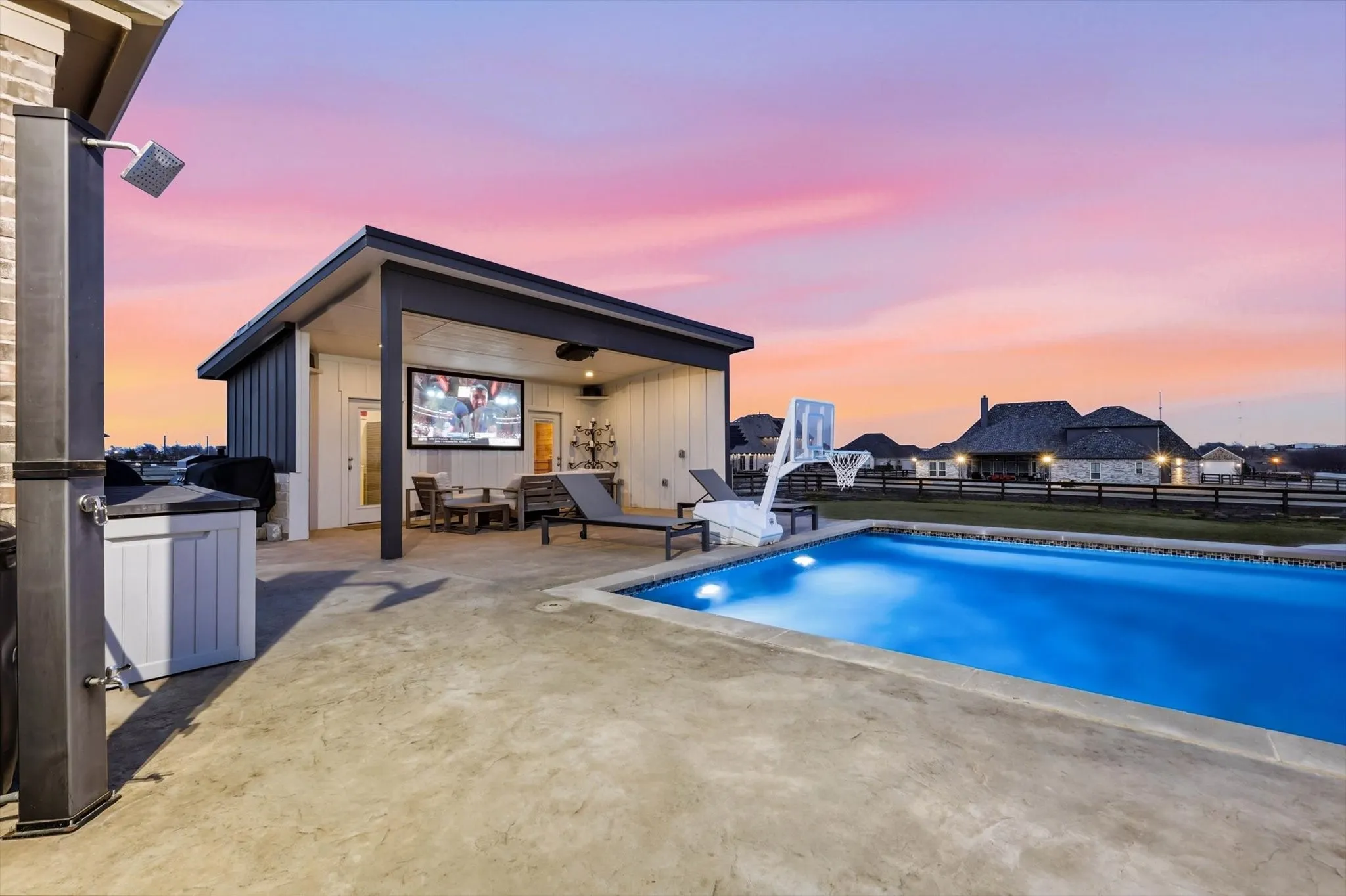 Outdoor living area featuring a rectangular swimming pool with integrated lighting, a pool house with a covered patio, an outdoor shower, and stamped concrete decking