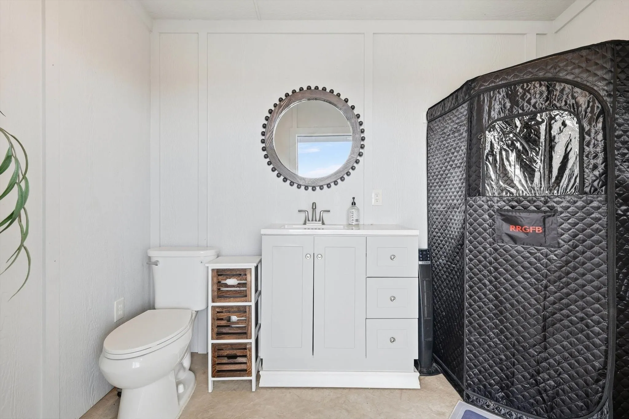 Bathroom featuring a vanity with a white countertop and gray cabinetry, a wall-mounted circular mirror, and board-and-batten style wall paneling