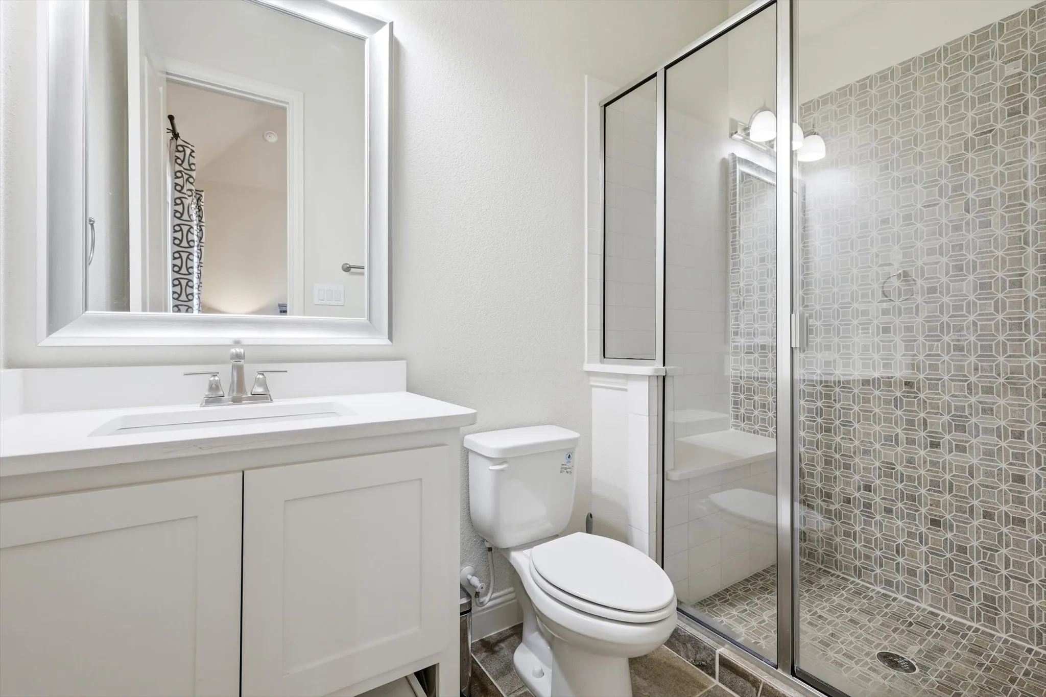 Bathroom featuring a white vanity with an integrated sink, brushed nickel faucet, framed mirror, toilet, and a glass-enclosed shower