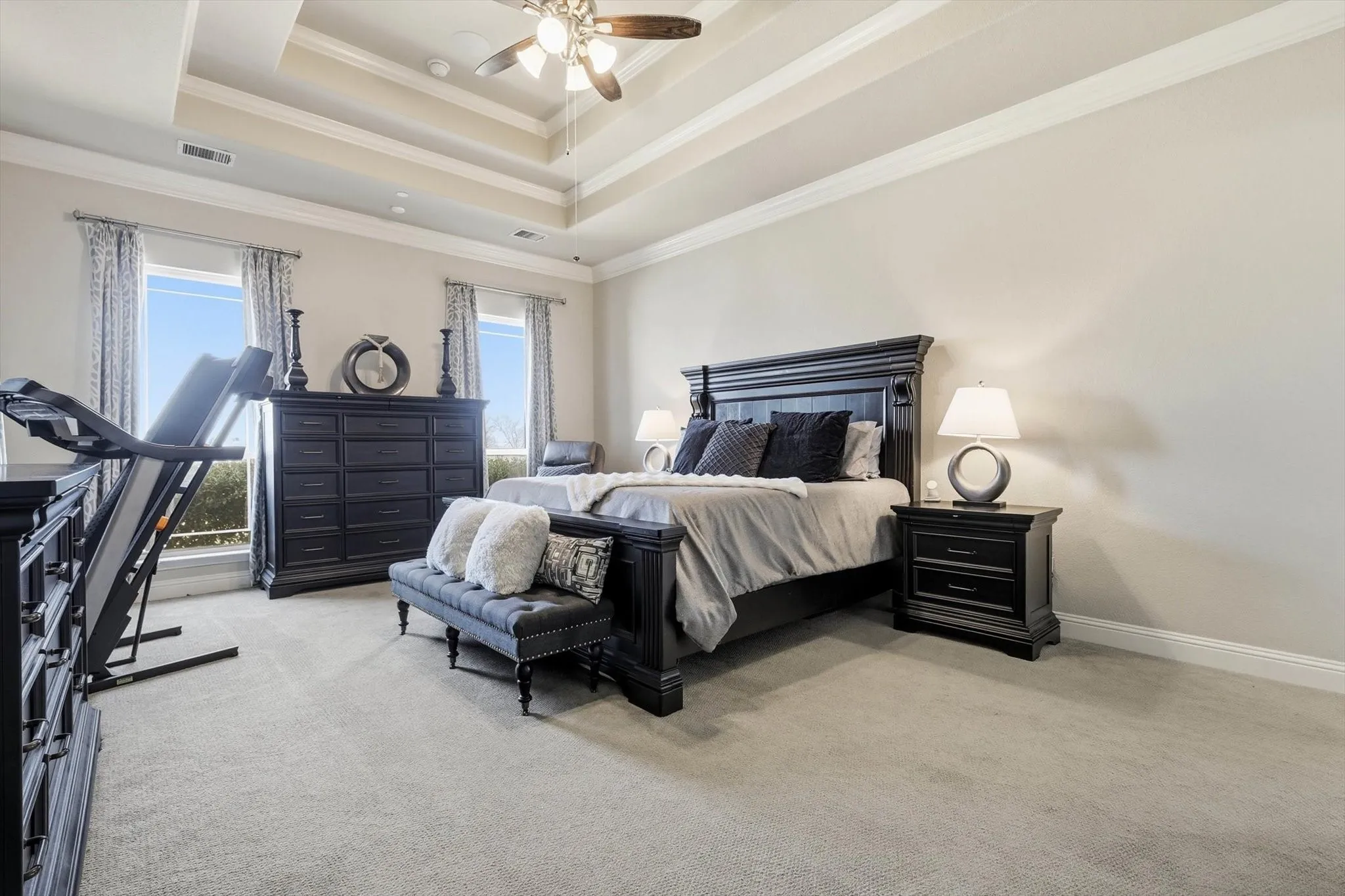 Spacious room featuring a tiered tray ceiling with a ceiling fan, light gray carpeting, and crown molding