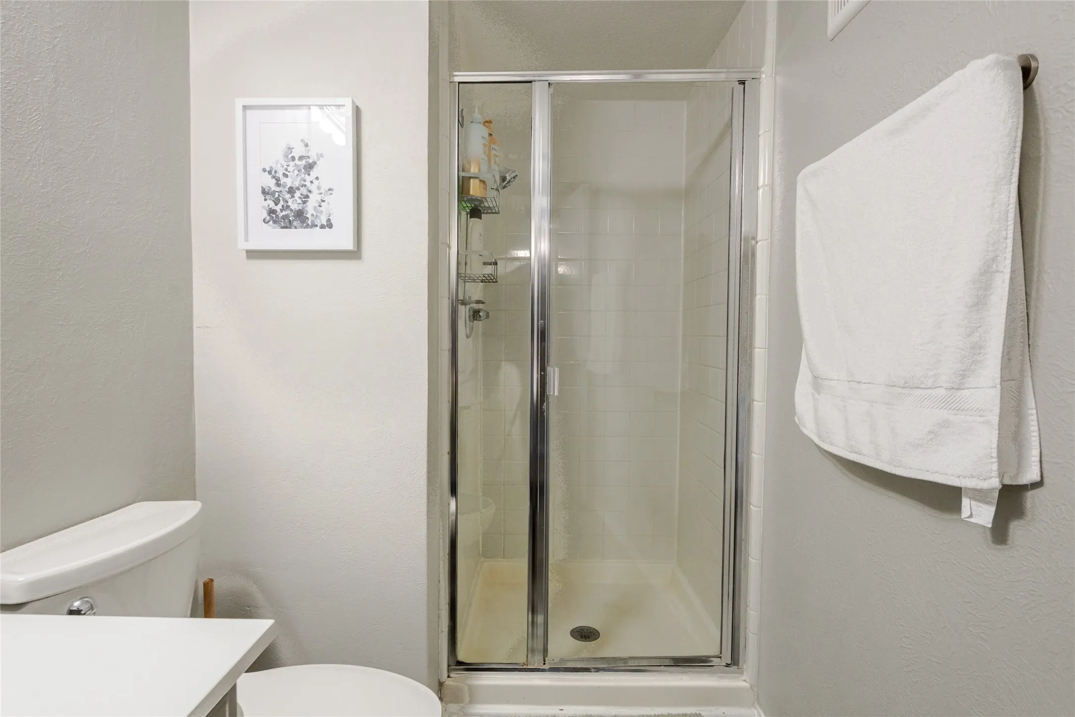 Enclosed shower with clear glass door, white tile surround, and chrome fixtures