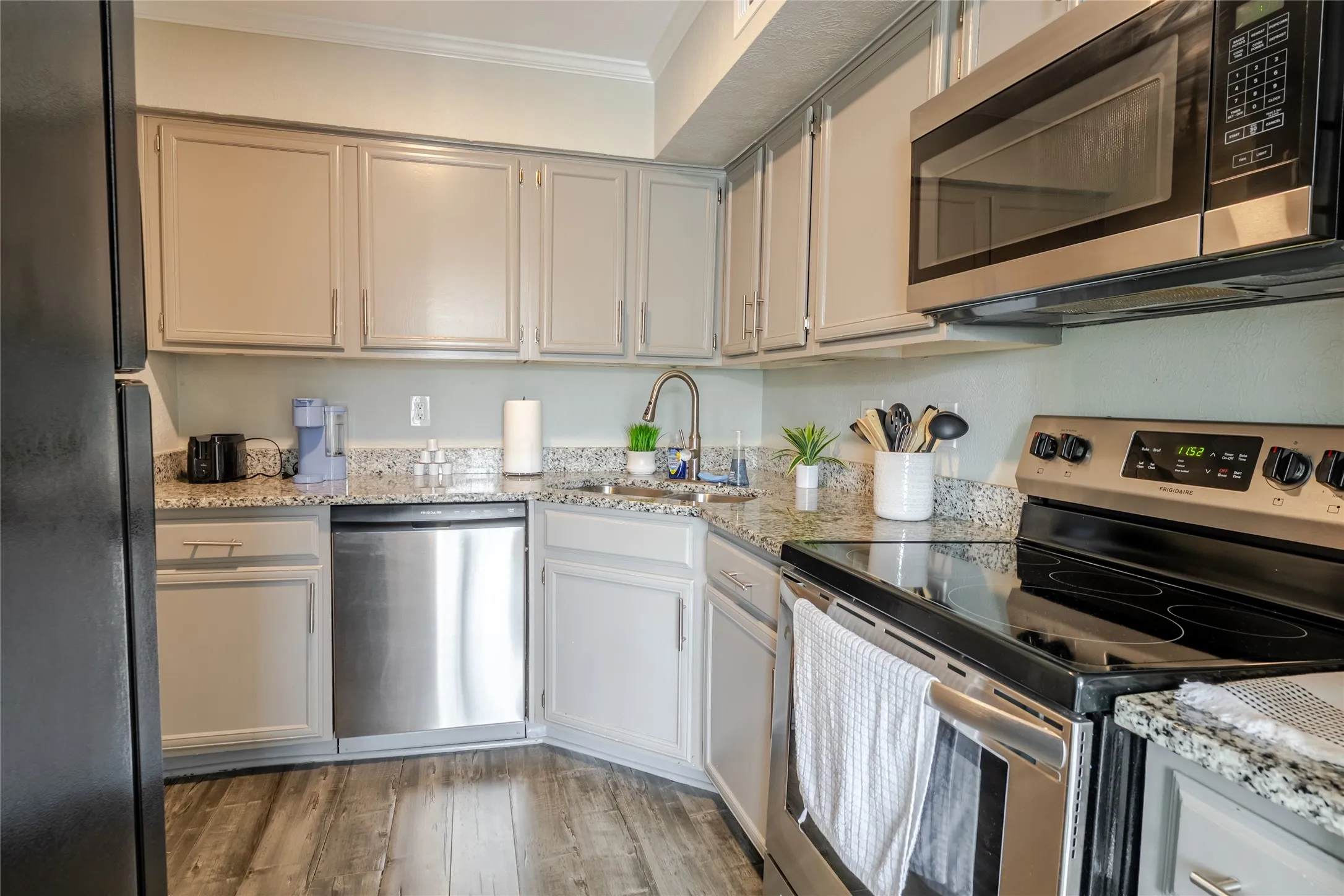 Kitchen featuring light-toned cabinetry, wood-finish flooring, stainless steel appliances, granite-style countertops, and a stainless steel sink with a gooseneck faucet