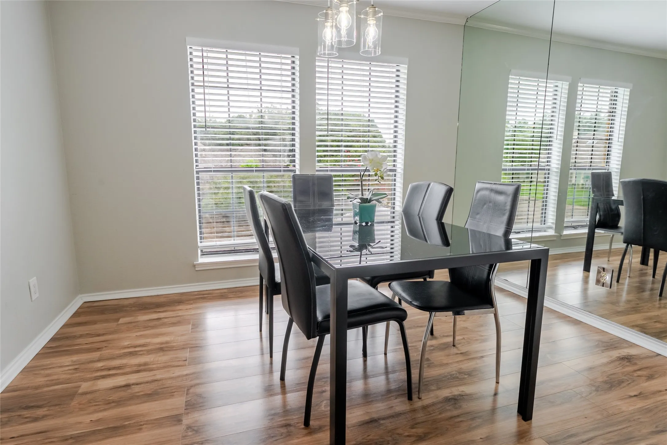 Dining area featuring wood-finish flooring, two large windows with blinds, a sleek overhead light fixture, and an expansive mirrored wall
