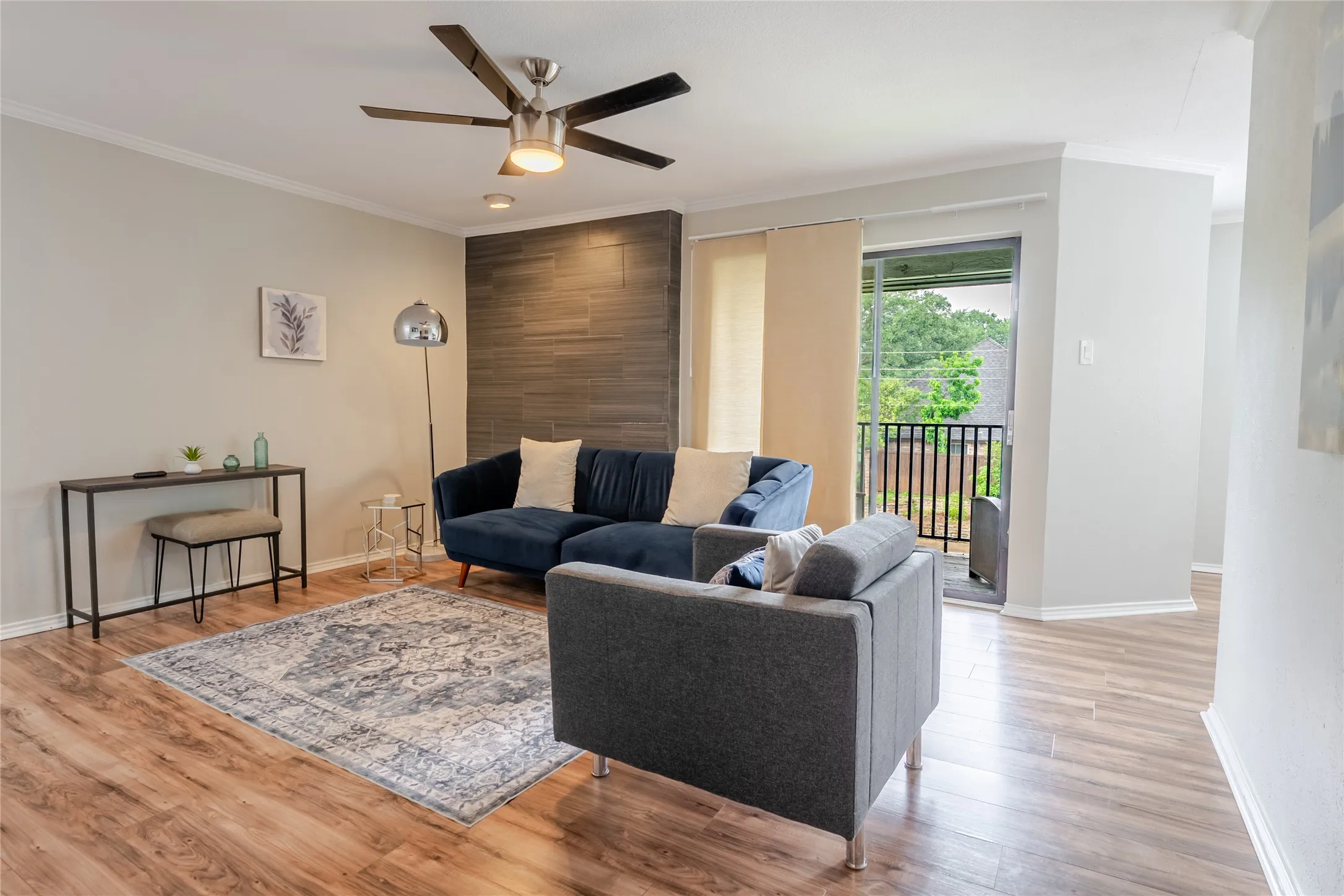 Living area featuring wood-finish flooring, a contemporary ceiling fan, and a floor-to-ceiling accent wall with horizontal tiling