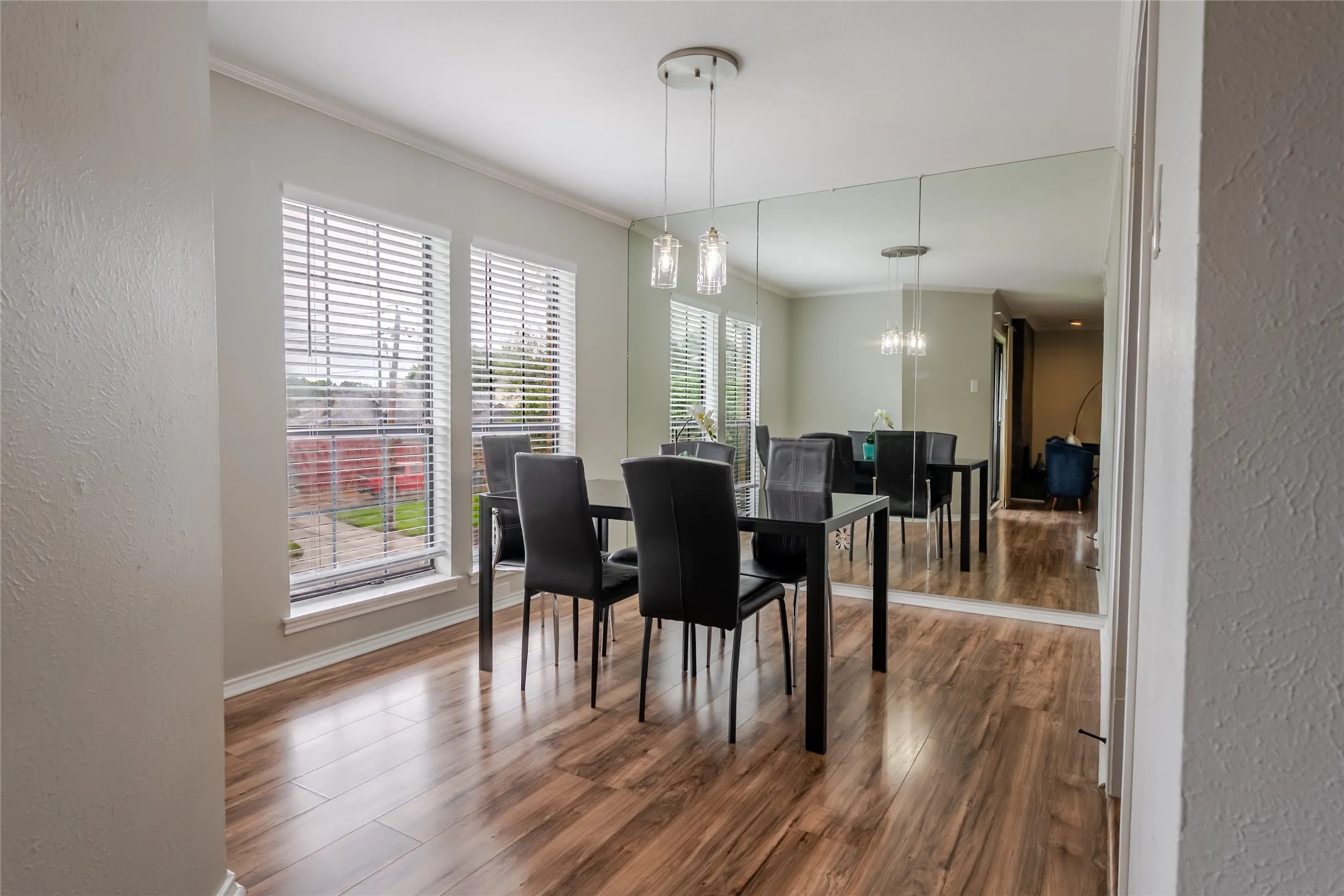 Dining area with wood-finish flooring, multiple windows, a ceiling-mounted light fixture, and a full-wall mirror
