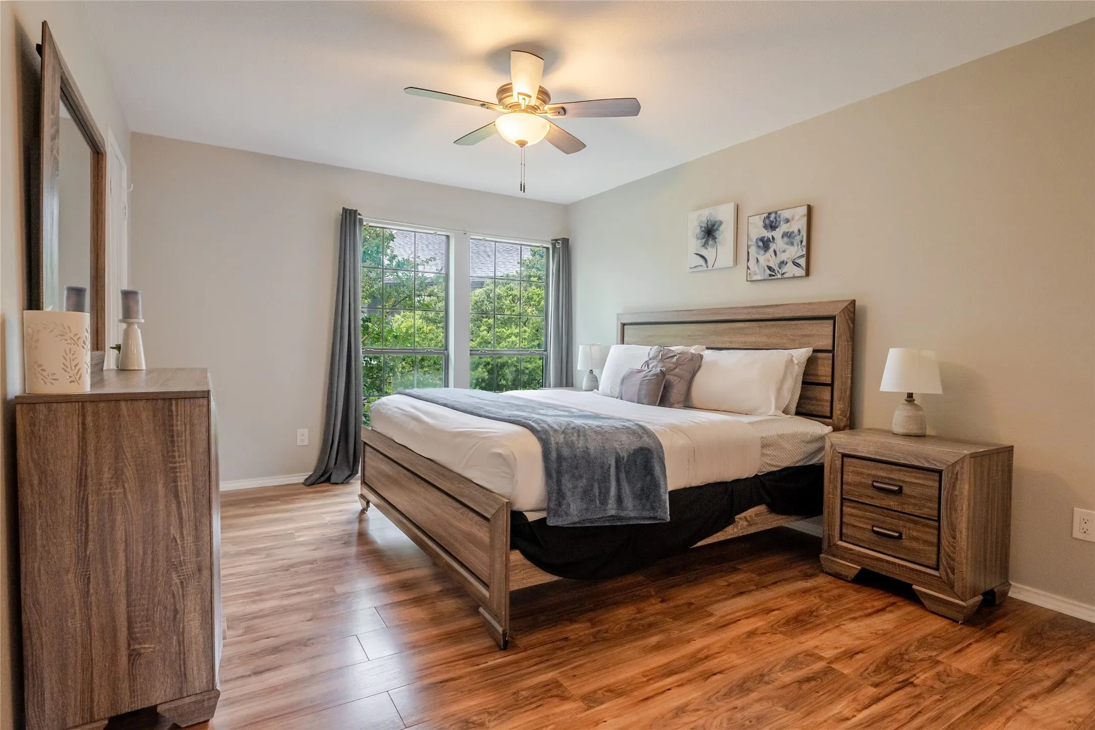 Spacious room featuring wood-finish flooring, a ceiling fan, and large windows providing abundant natural light