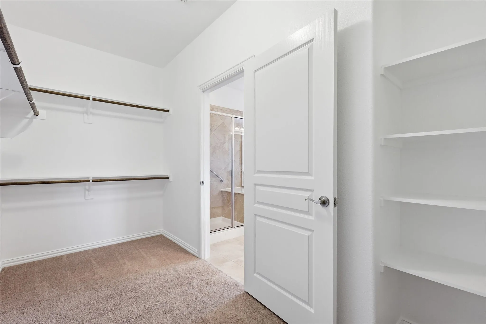 Spacious closet featuring two levels of hanging rods, built-in shelving, and neutral carpeting