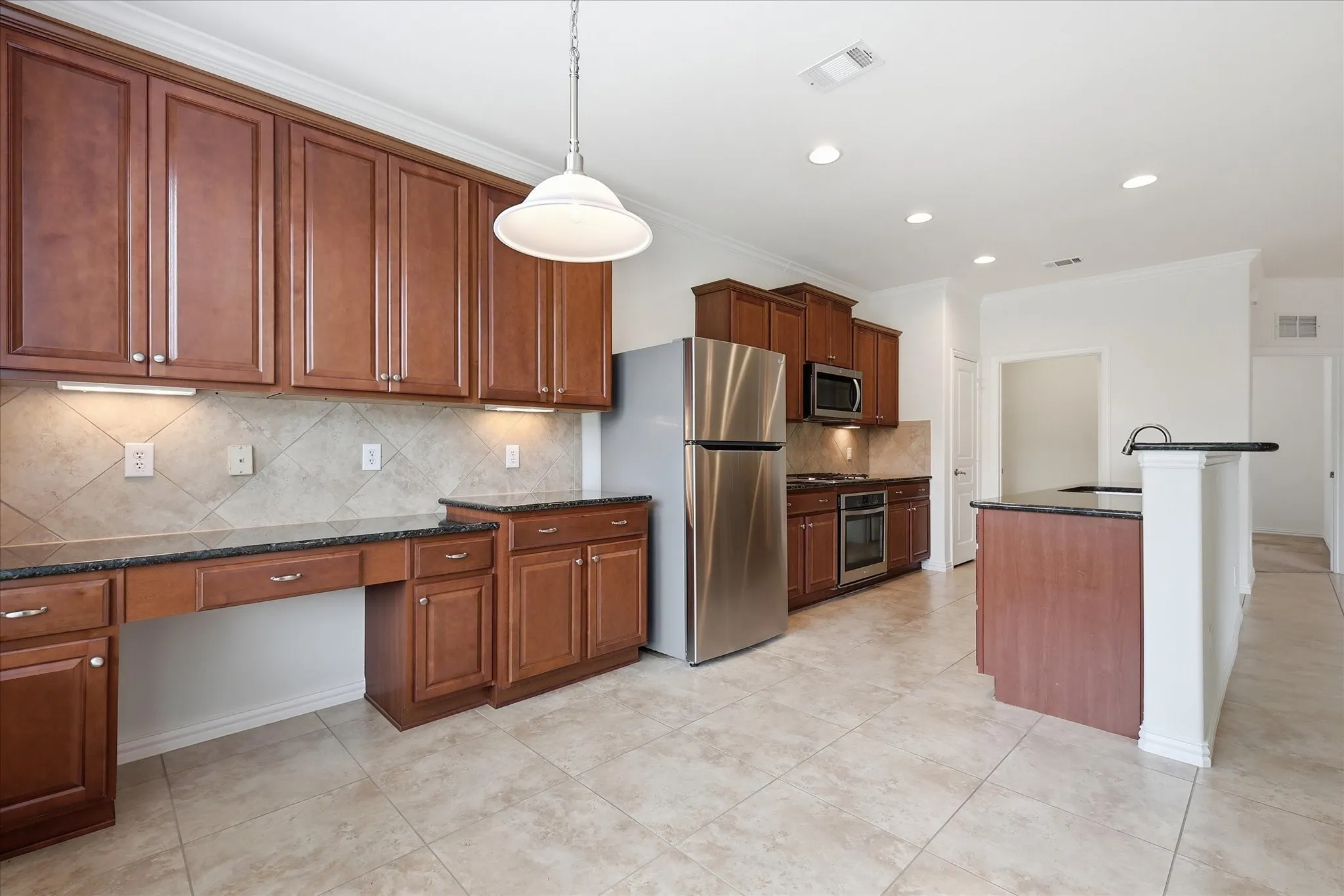 Spacious kitchen featuring rich wood-finish cabinetry, dark countertops, a tile backsplash, stainless steel appliances, and tile flooring