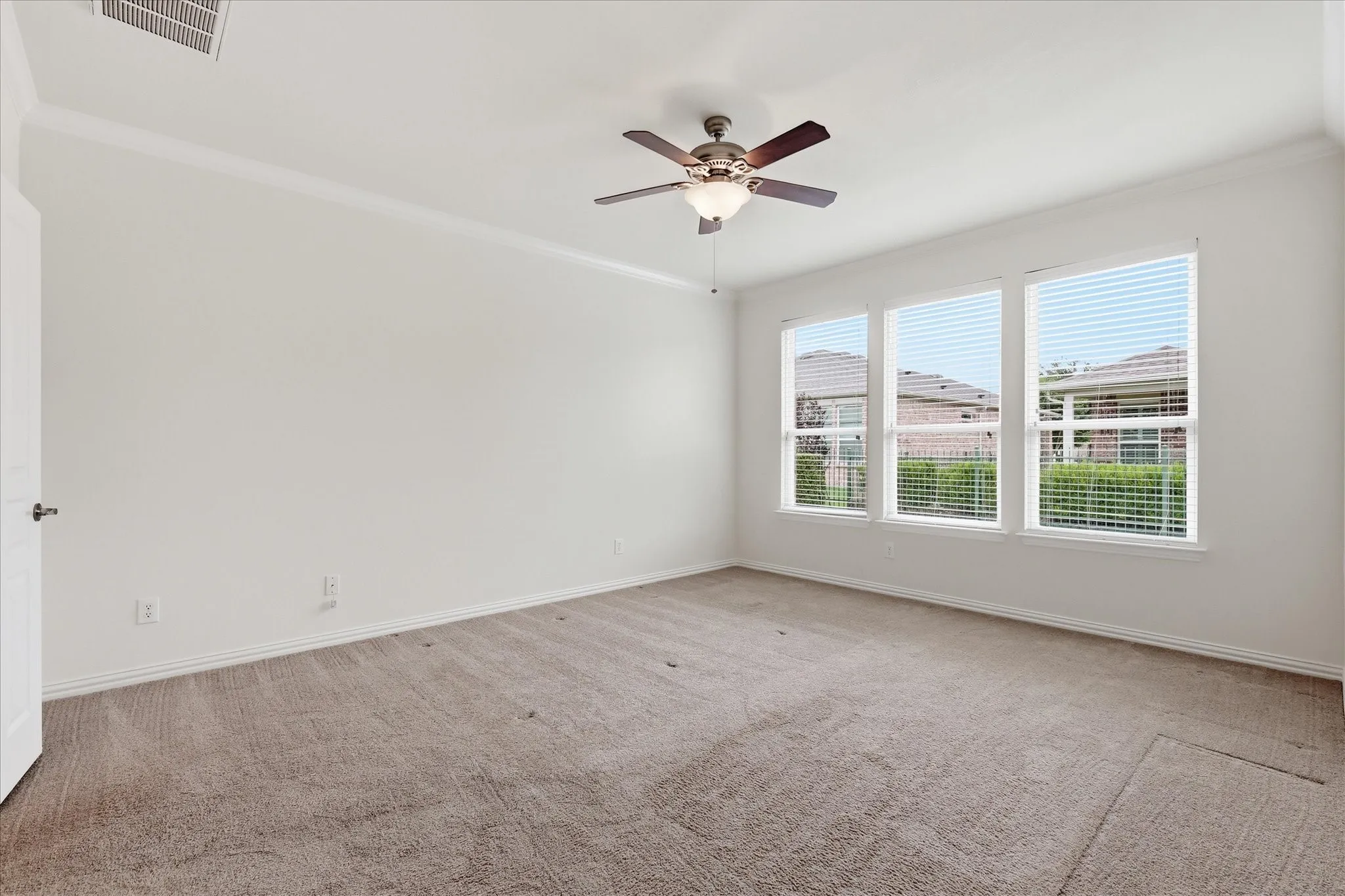 Spacious room featuring multiple windows with horizontal blinds, neutral carpeting, and a ceiling fan with integrated lighting