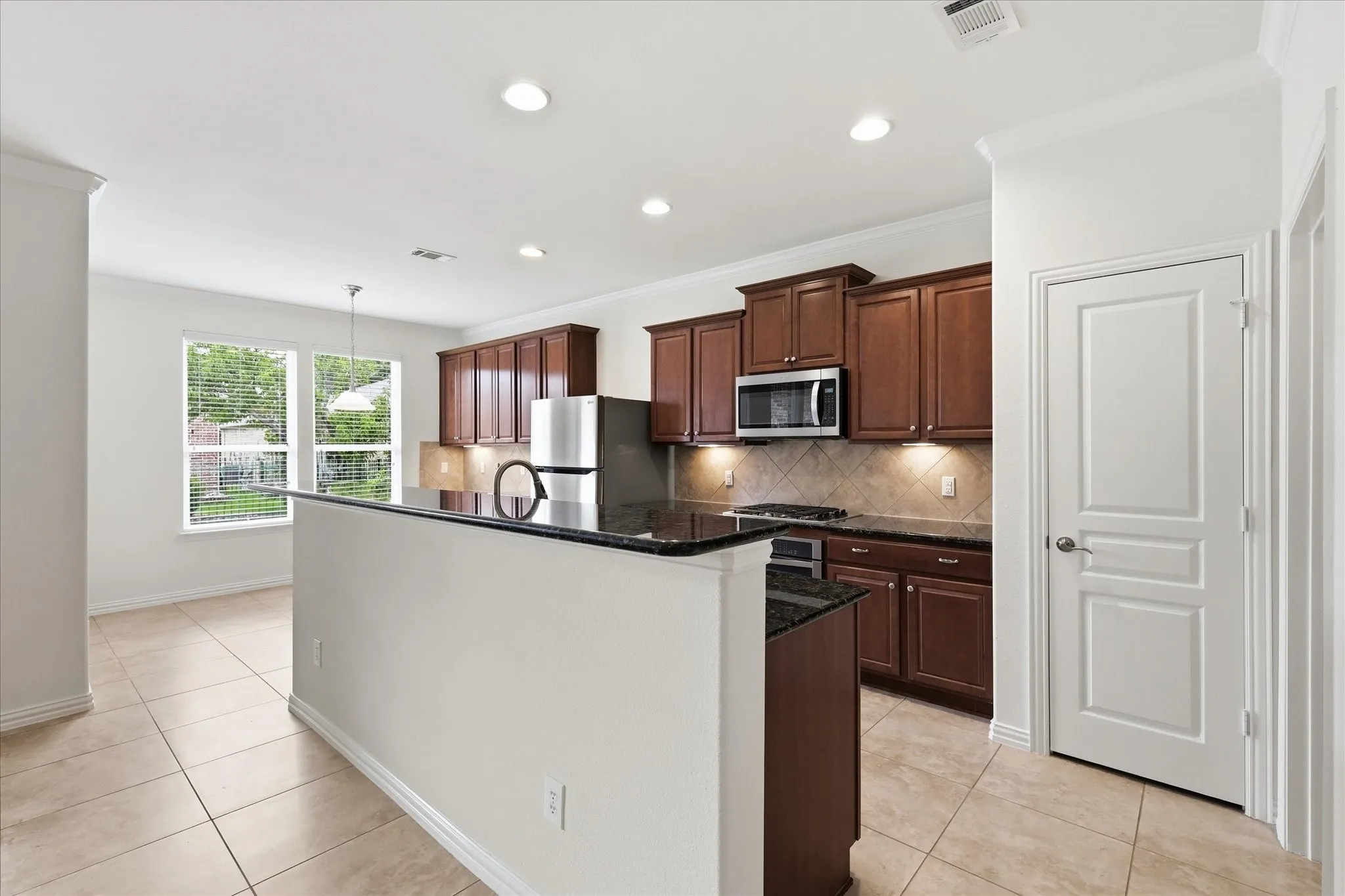Kitchen featuring an island with a black countertop, wood cabinetry, stainless steel appliances, and recessed lighting