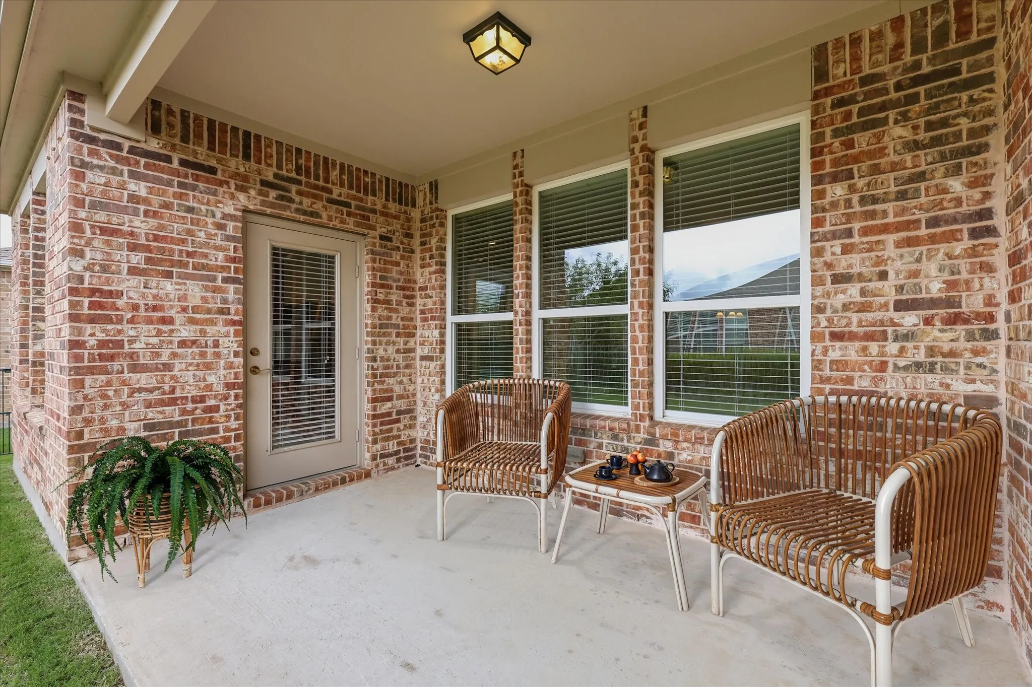 Covered patio featuring a concrete slab, brick exterior, two windows with blinds, and a glass-paneled door