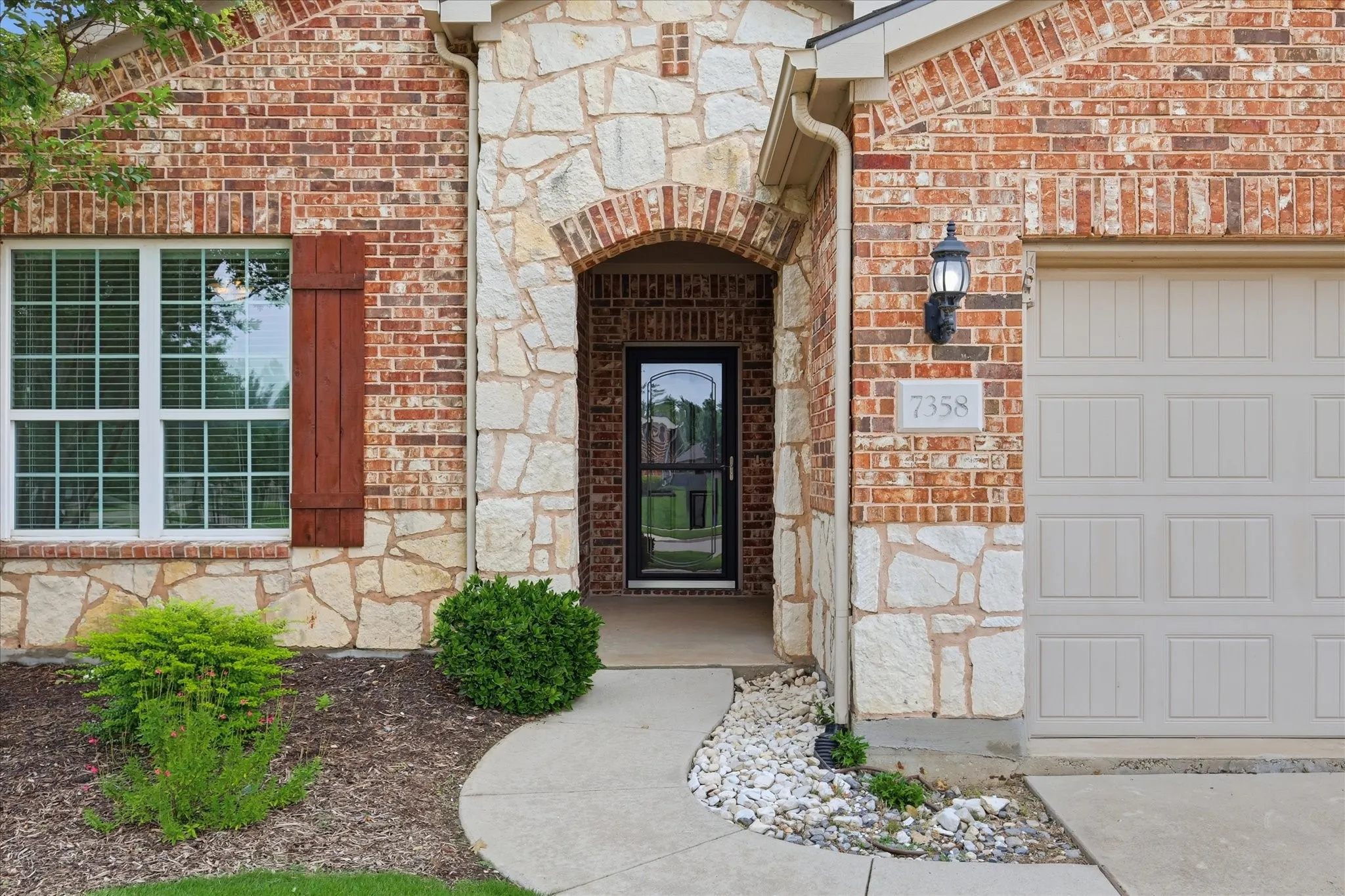 Brick and stone veneer exterior featuring an arched entryway with a glass storm door