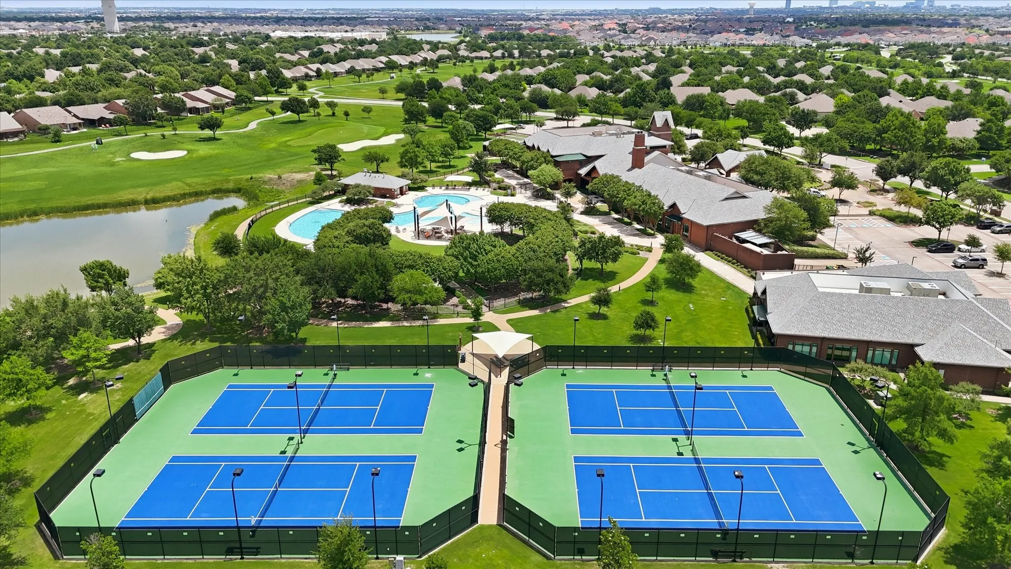 Aerial perspective showcasing multiple tennis courts with blue playing surfaces and green surrounds, bordered by fencing