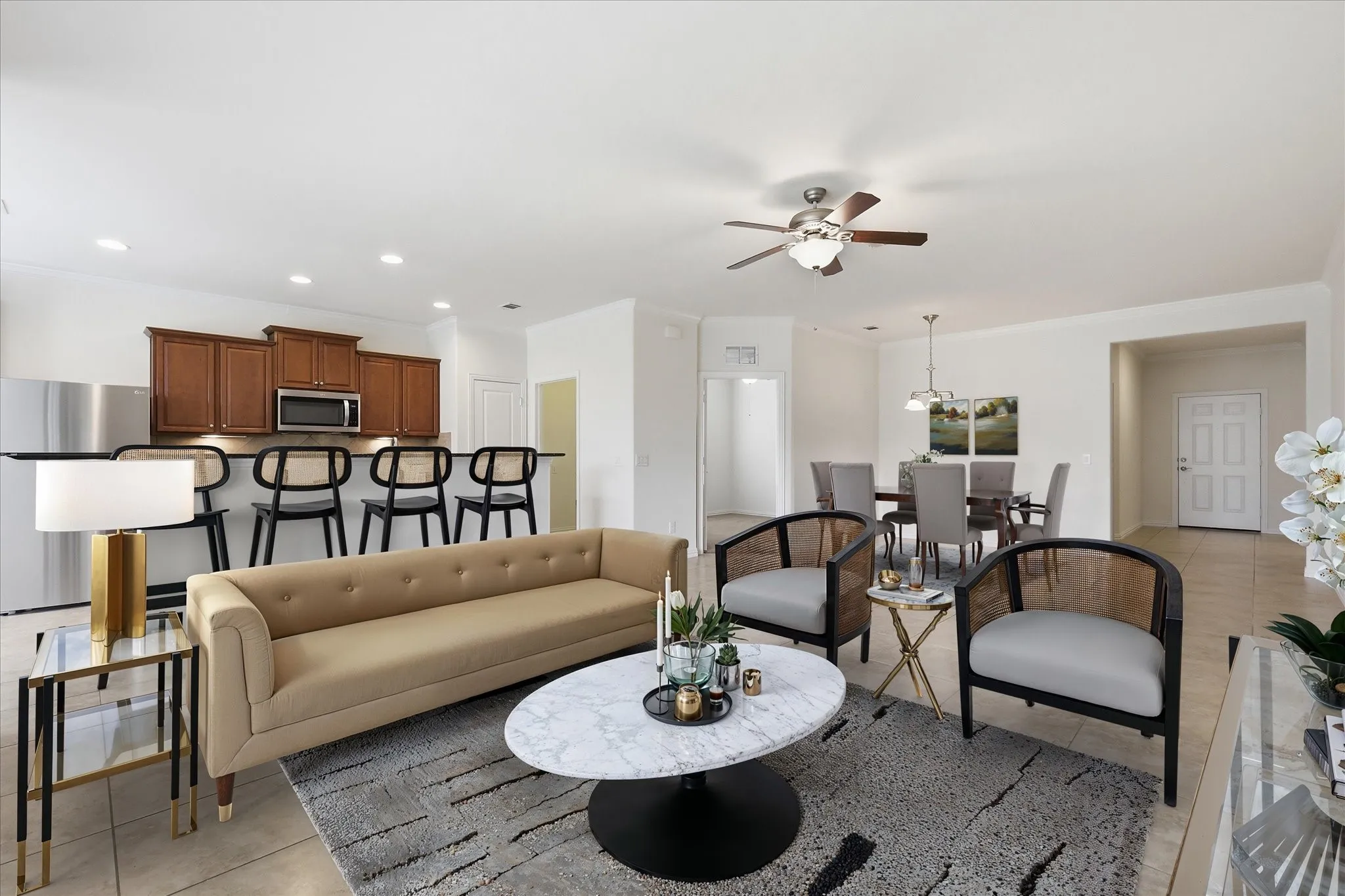 Staged Open-concept interior featuring light-toned tile flooring, a kitchen island with seating, dark wood cabinetry, and stainless steel appliances