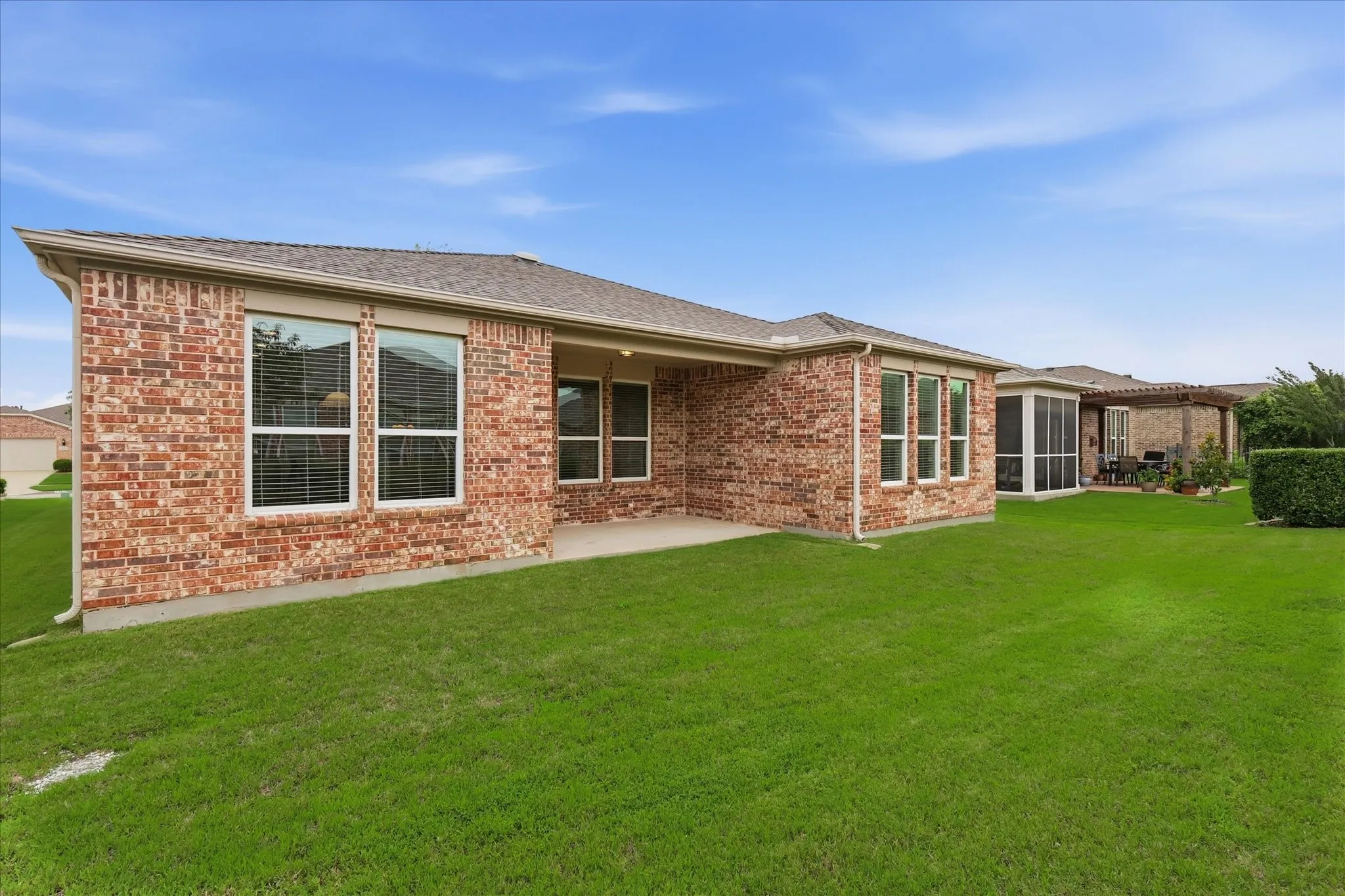 Expansive green lawn surrounds a brick exterior featuring multiple windows and a covered patio