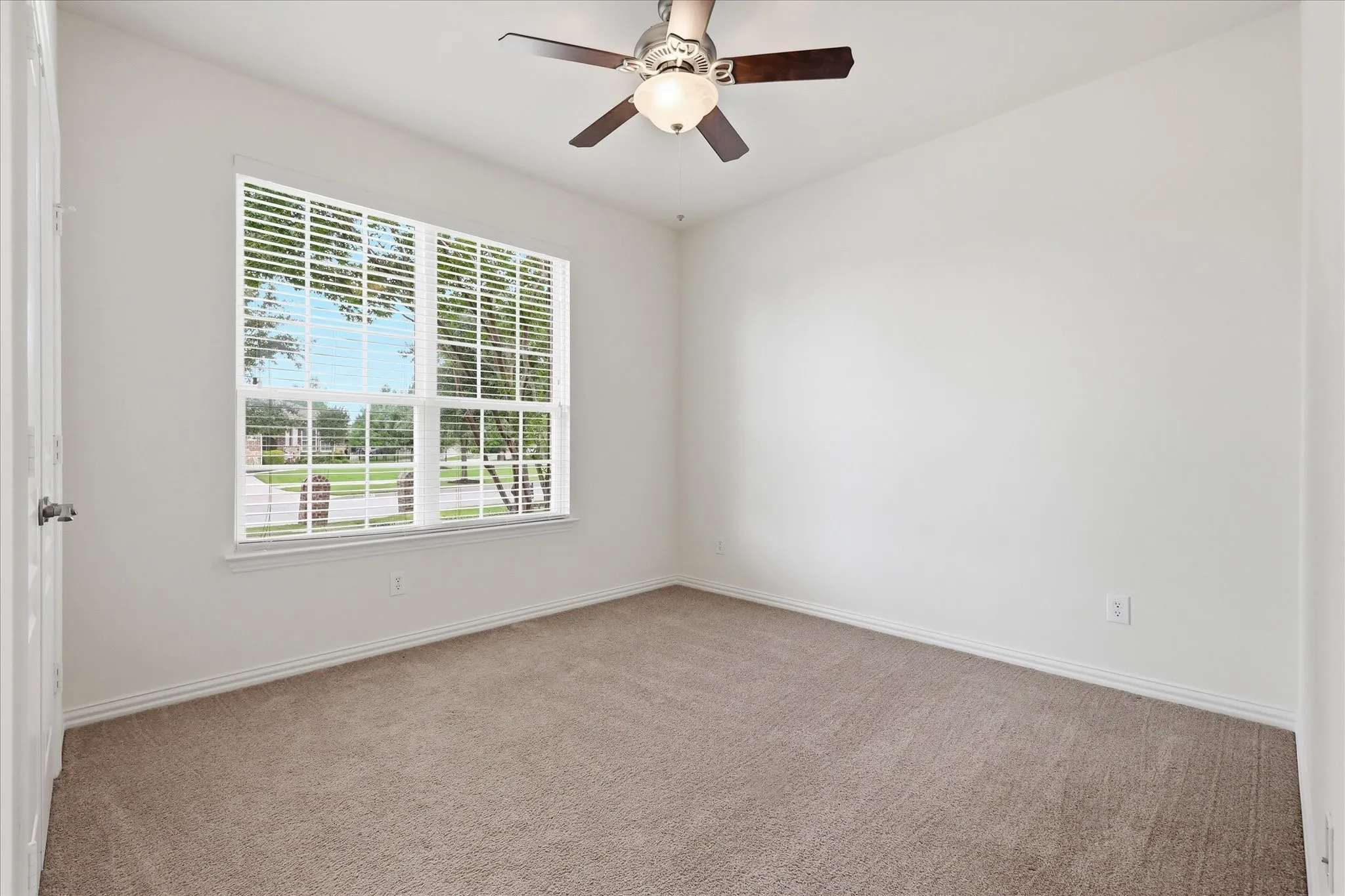 Bright interior space with a large window, neutral carpeting, and a ceiling fan with integrated lighting