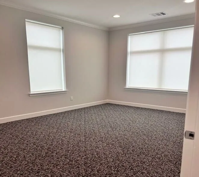 Spacious room featuring patterned carpet flooring, two windows with roller shades, recessed lighting, and crown molding