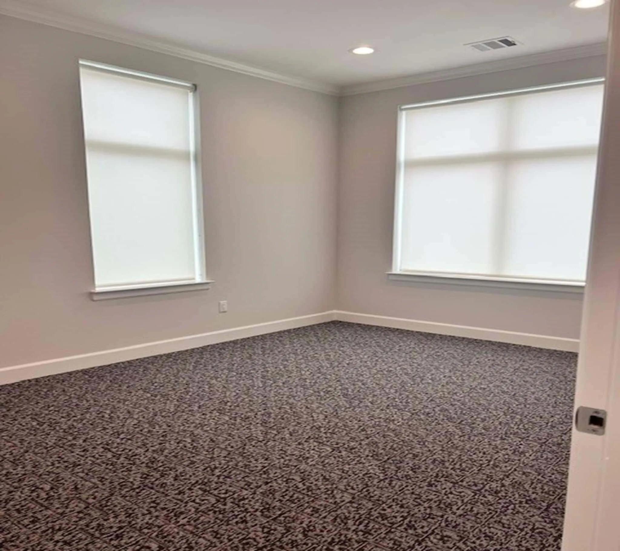 Room featuring patterned carpet flooring, recessed lighting, crown molding, and two windows with roller shades