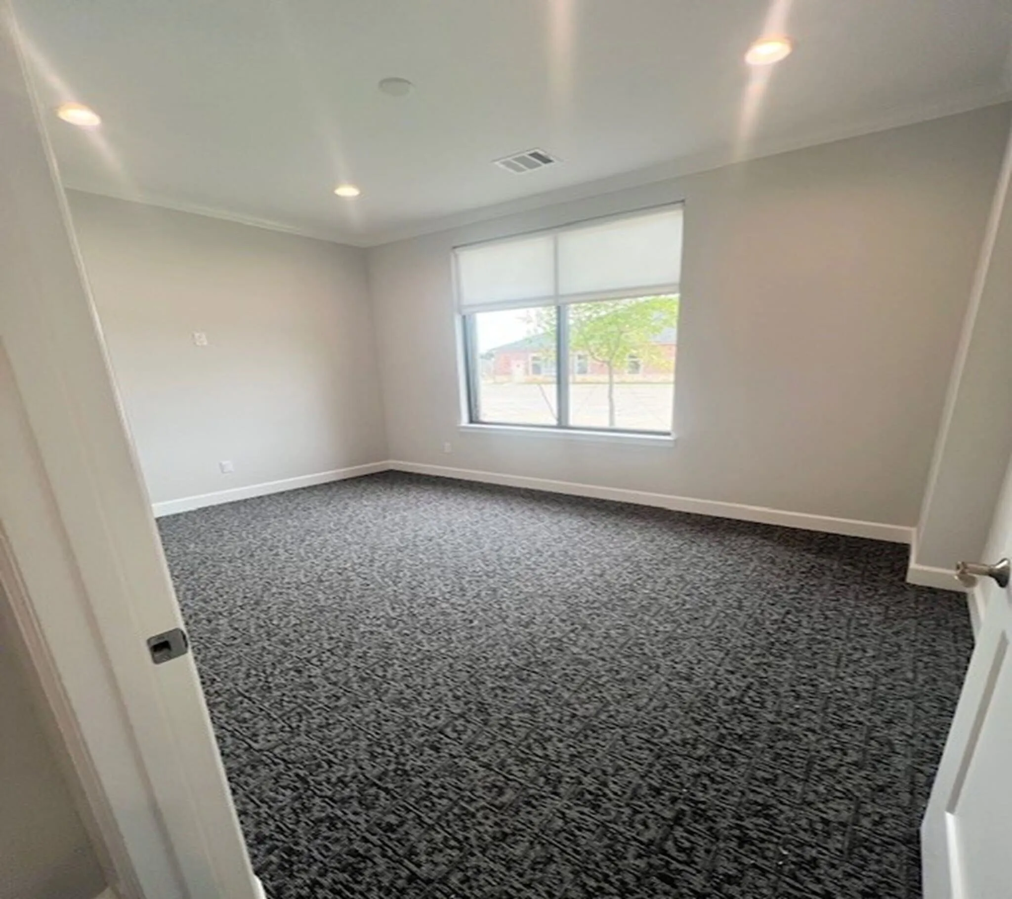 Spacious room featuring patterned carpet flooring, recessed lighting, a large window with roller shades, and crown molding