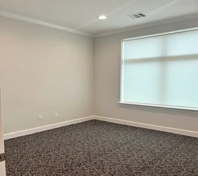 Bright room featuring a large window with roller shades, recessed lighting, crown molding, and textured carpeting