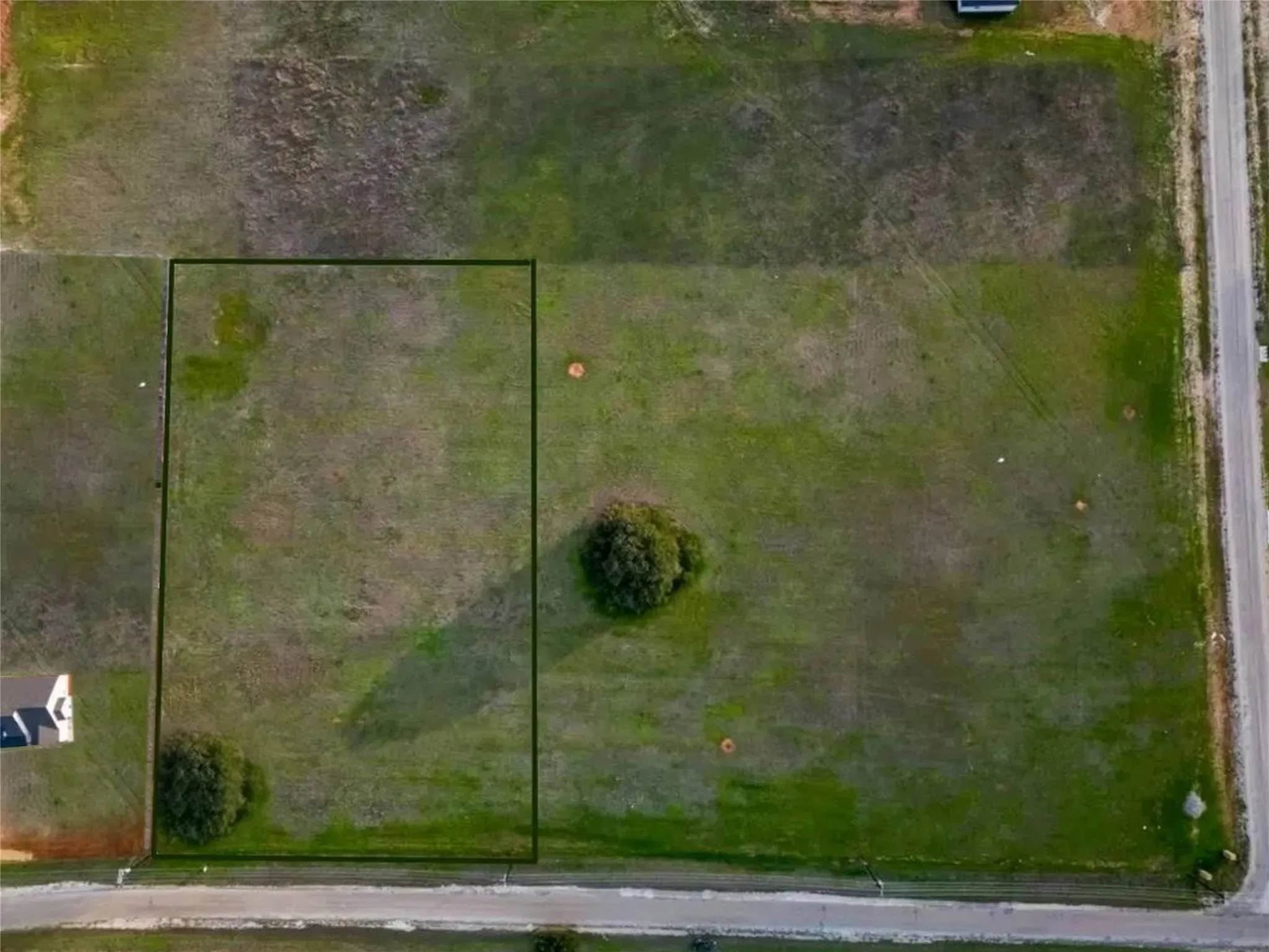 Expansive rectangular land parcel featuring a grass and dirt surface, bordered by a paved road