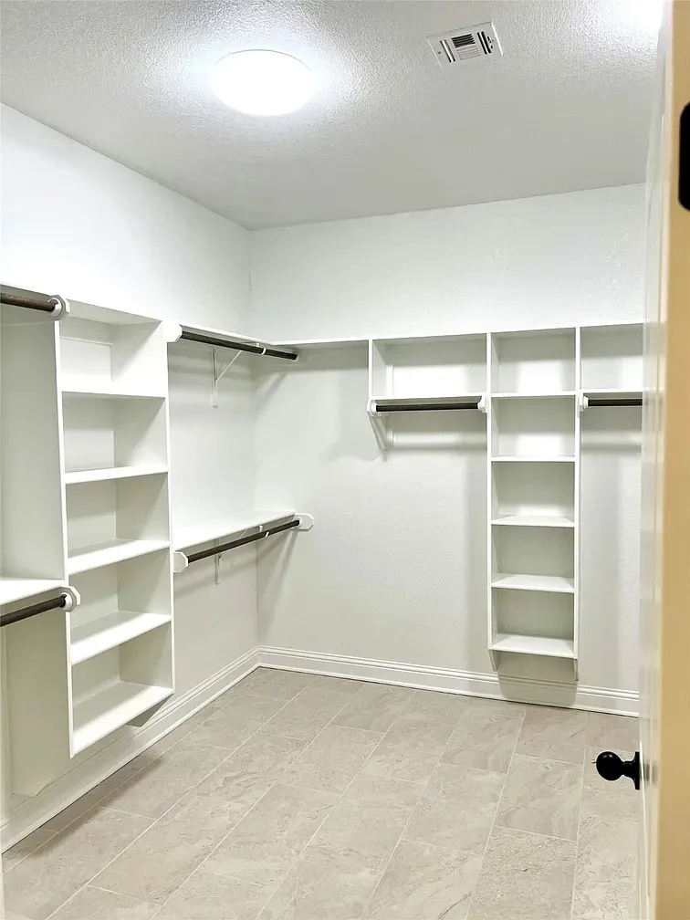 Expansive walk-in closet featuring light-toned tile flooring, built-in shelving, and multiple hanging rods