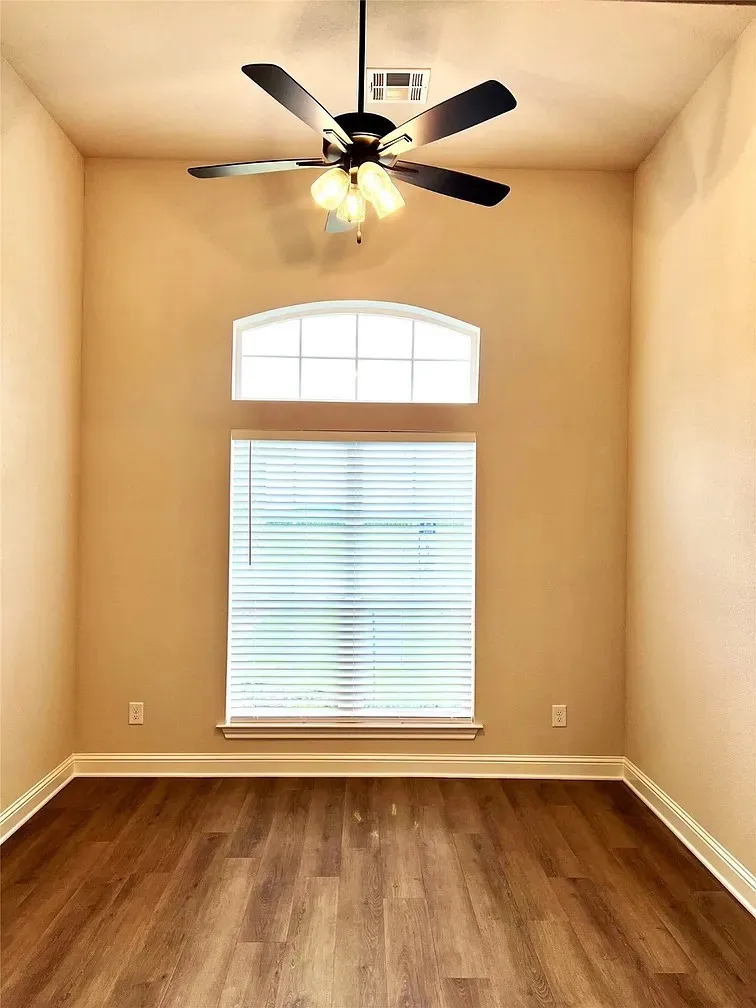 Spacious room featuring vaulted ceilings, wood-finish flooring, a contemporary ceiling fan with integrated lighting, and a combination of arched and rectangular windows