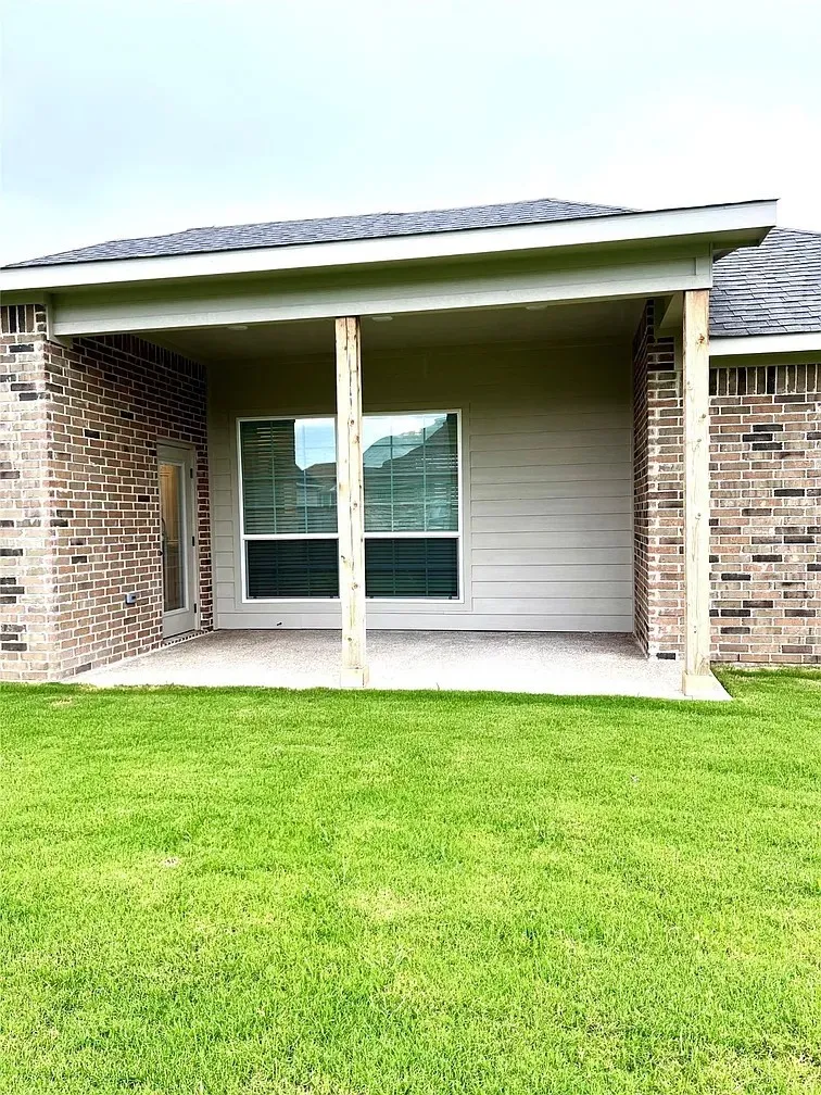 Covered patio with a concrete slab, supported by two wooden posts, extending from the rear of the brick exterior