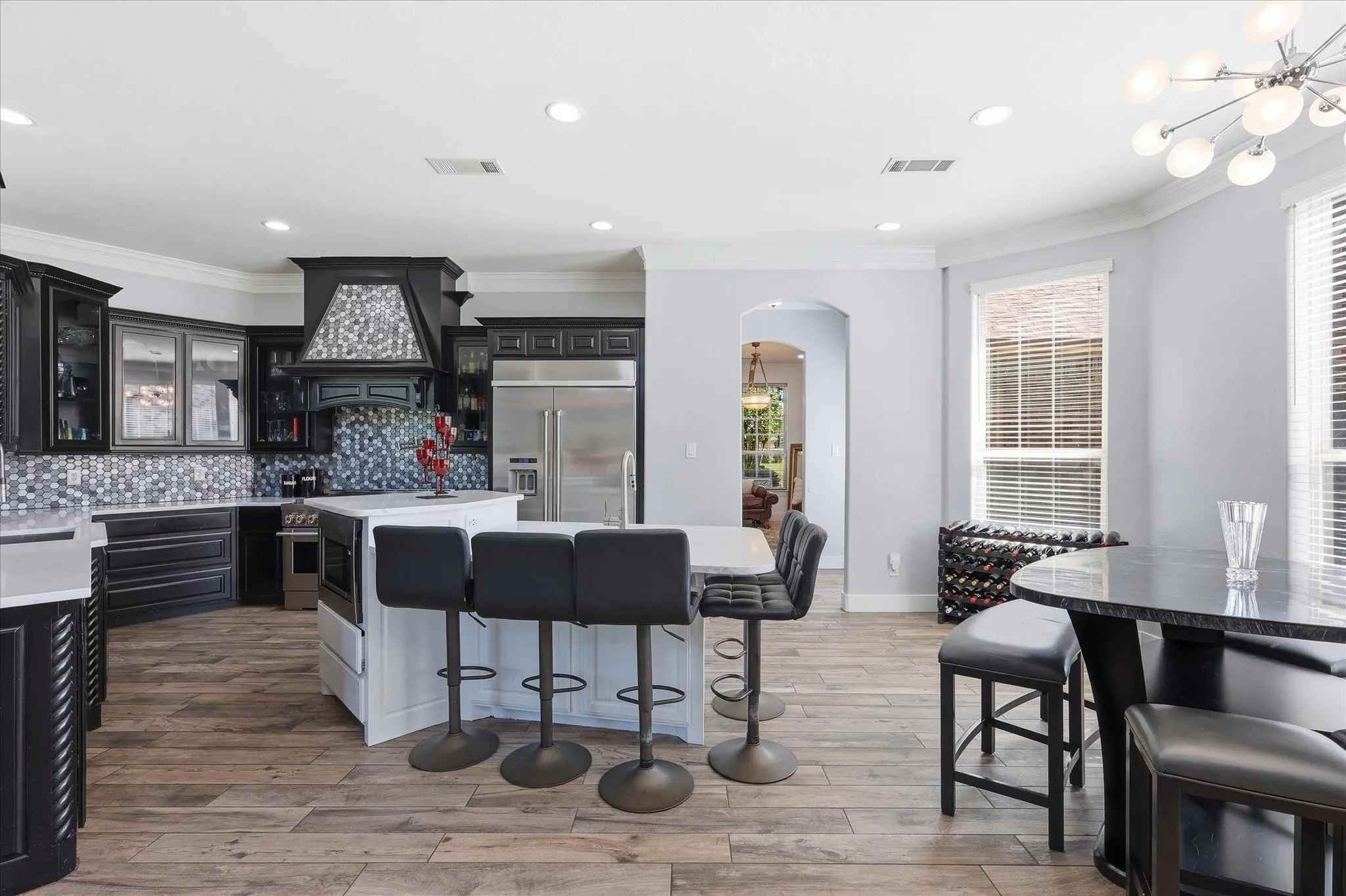 Modern kitchen featuring dark cabinetry, stainless steel appliances, a mosaic tile backsplash, a white island with bar seating, and wood-finish flooring