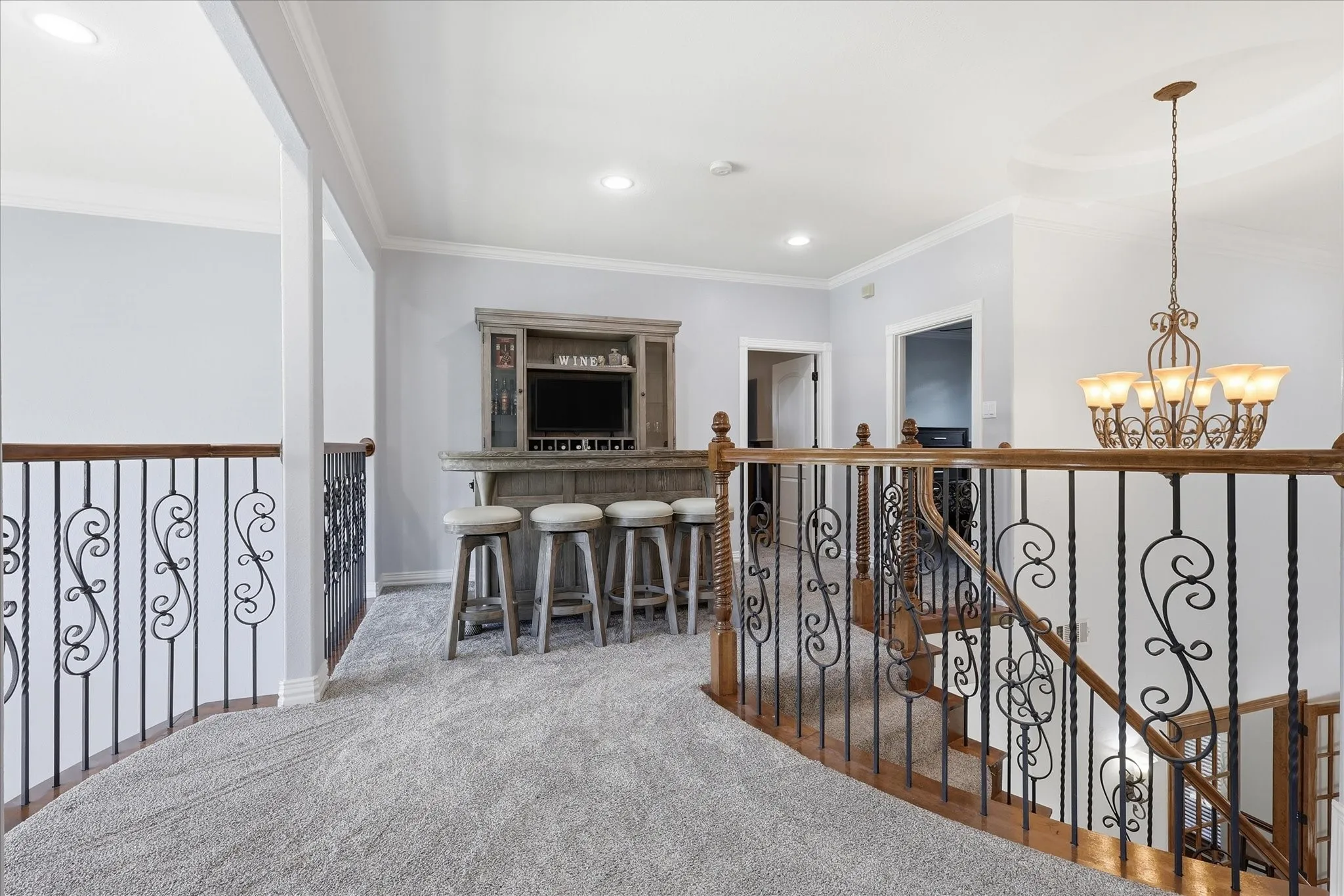 Upper-level landing featuring a built-in bar with seating, carpeted flooring, wrought iron and wood balusters, recessed lighting, and a decorative chandelier
