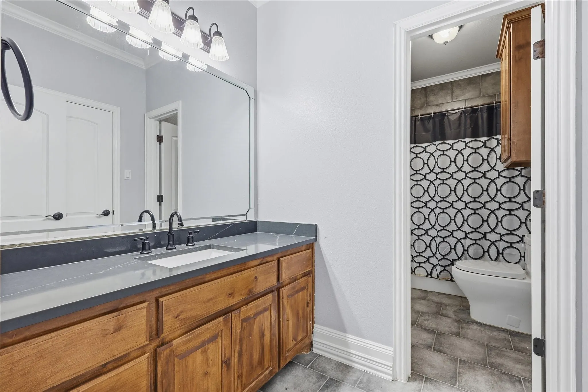 Bathroom vanity featuring a quartz countertop, matte black faucet, and a light wood-finish cabinet with multiple storage doors