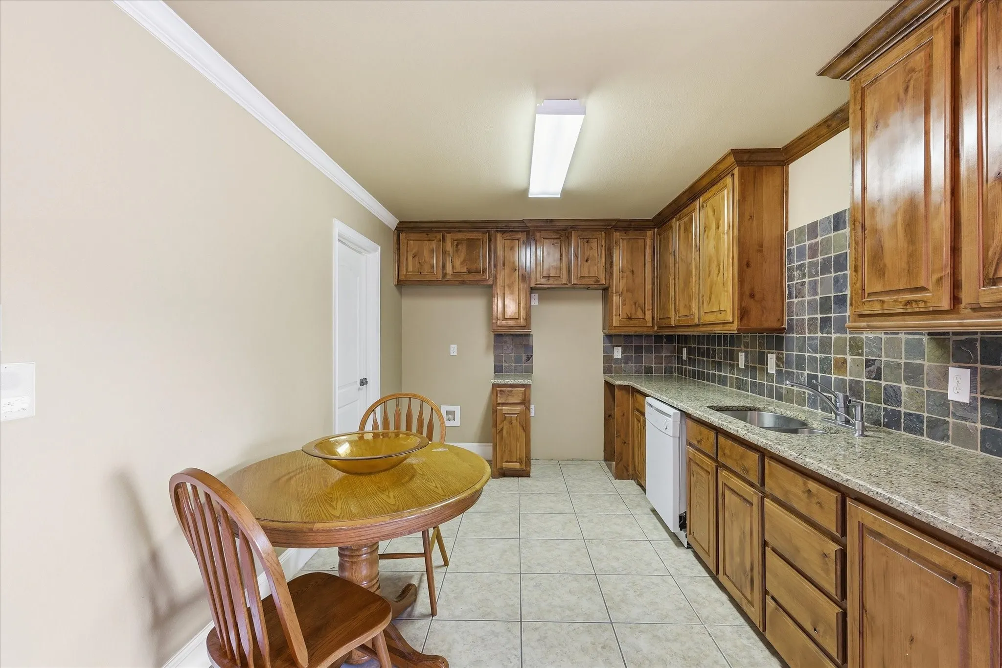 Kitchen featuring wood cabinetry, stone-look tile backsplash, light granite-style countertops, and tile flooring