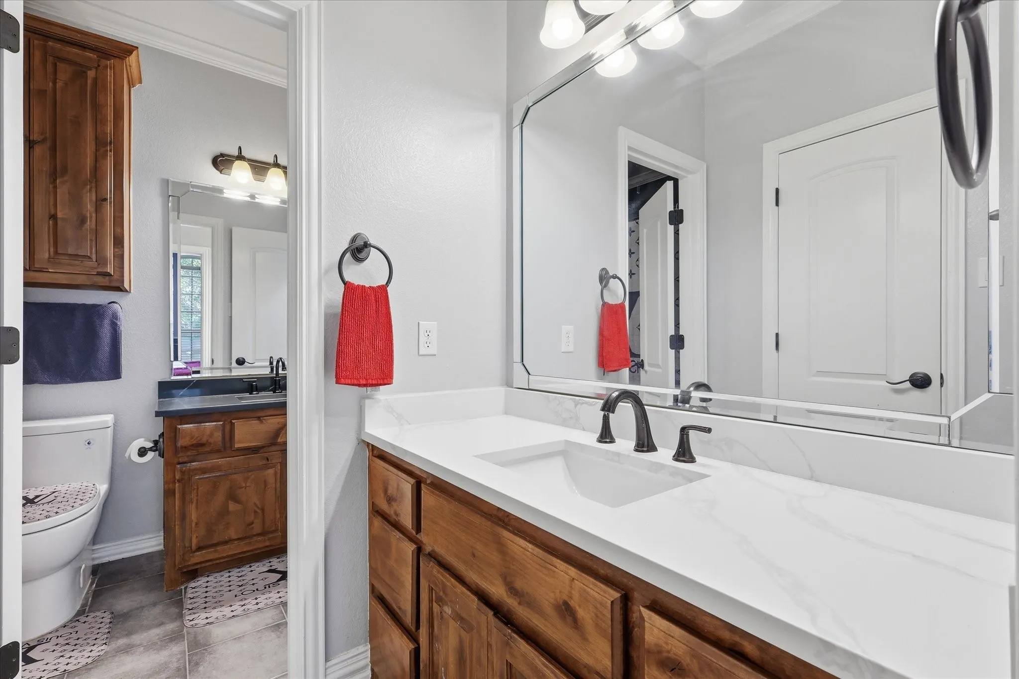 Bathroom featuring a spacious vanity with a white countertop and integrated sink, rich wood-tone cabinetry, and a large wall-mounted mirror