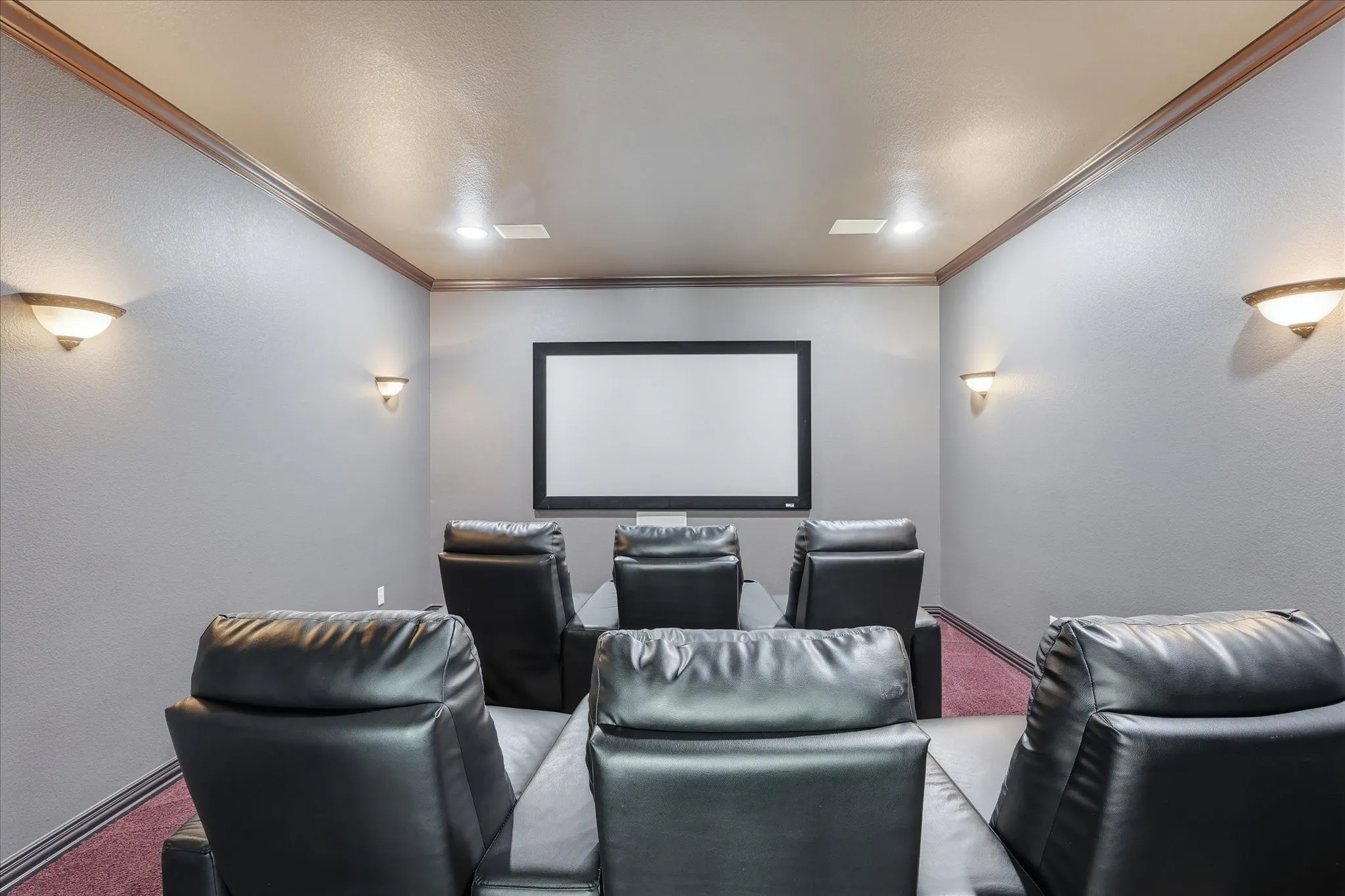 Dedicated home theater featuring a large projection screen, dark textured walls, brown crown molding, and recessed lighting