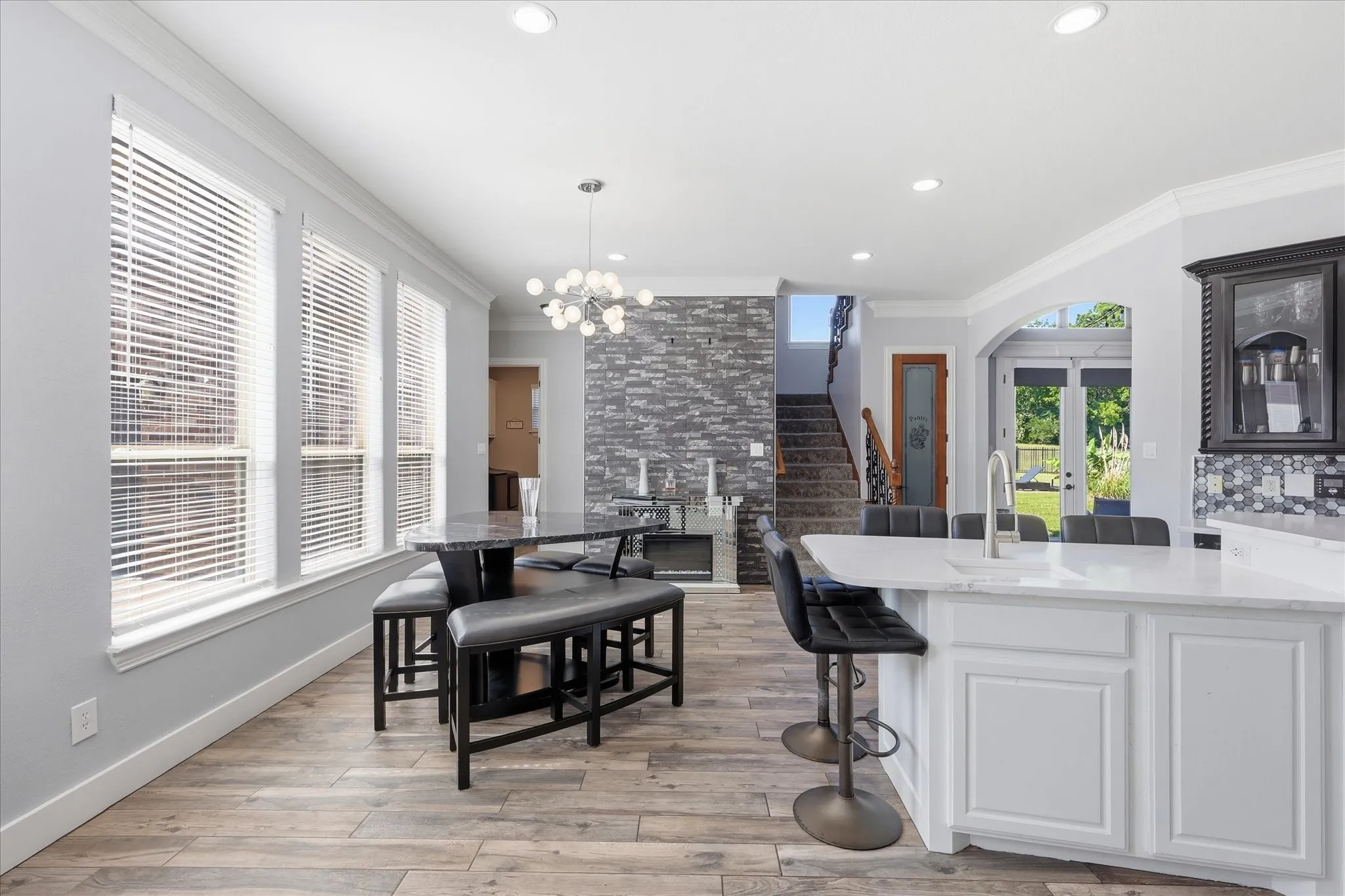 Open-concept living space featuring wood-finish flooring, a contemporary kitchen island with a double basin sink, white cabinetry, and a dark stone accent wall with a built-in fireplace