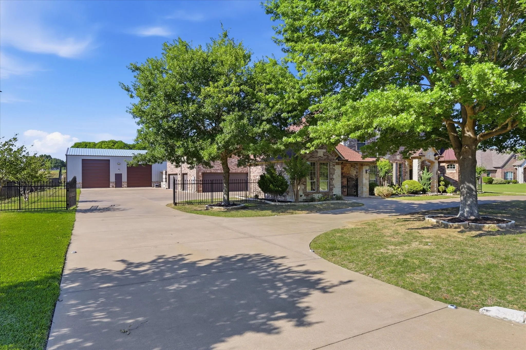 Expansive concrete driveway leading to a stone and brick facade residence with a separate metal building