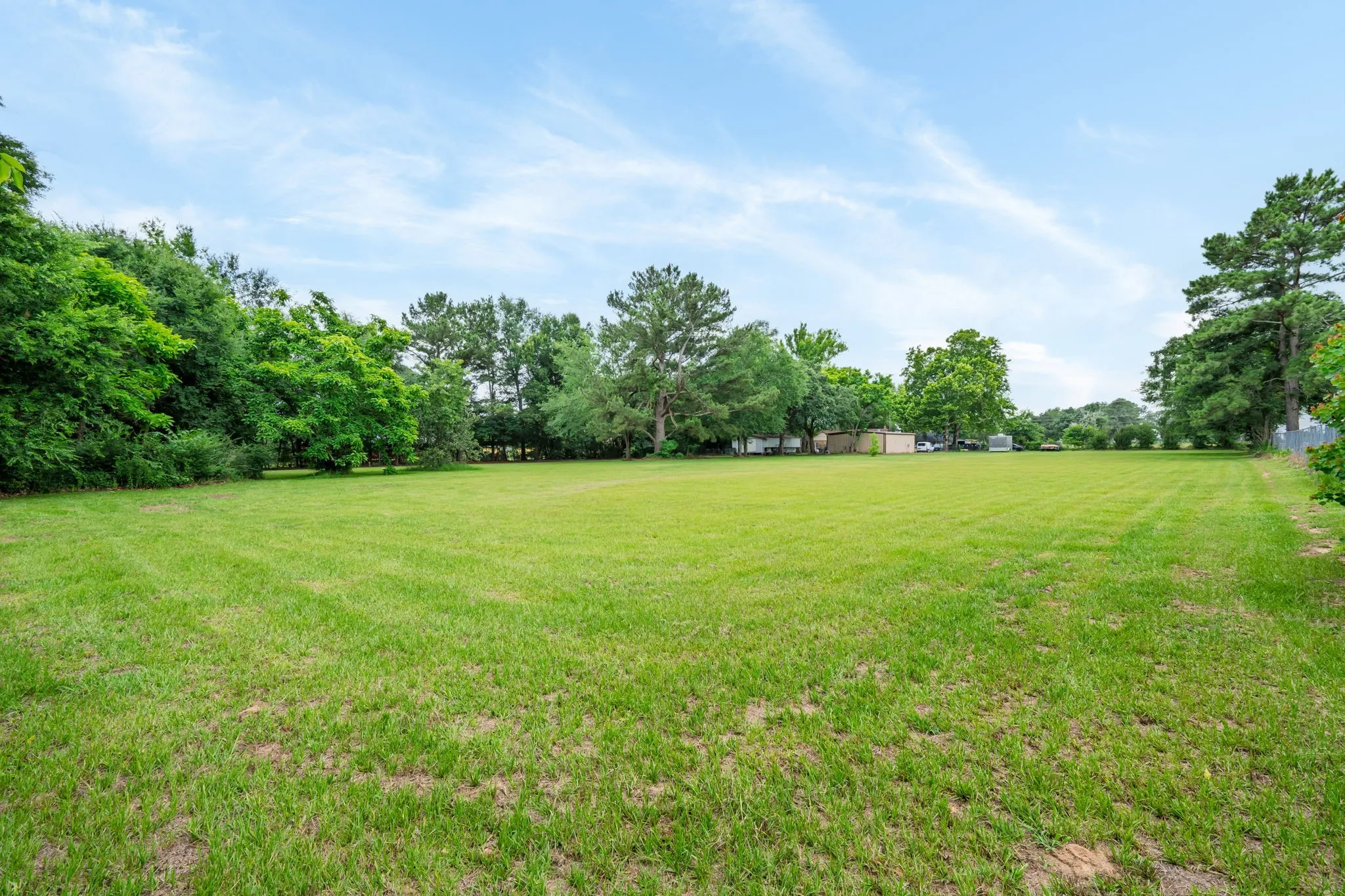 Expansive grassy lot featuring mature perimeter trees and clear skies