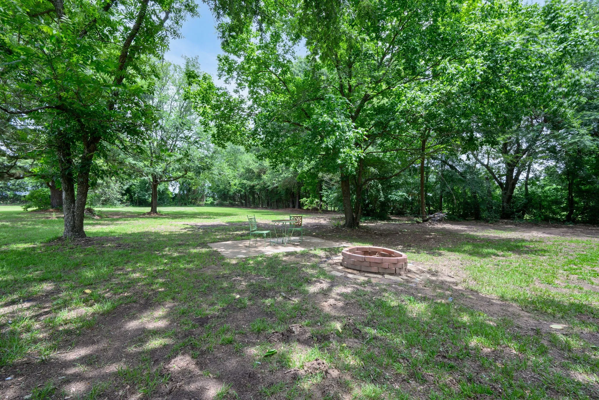 Expansive outdoor space featuring mature trees, a circular brick fire pit, and a grassy lawn