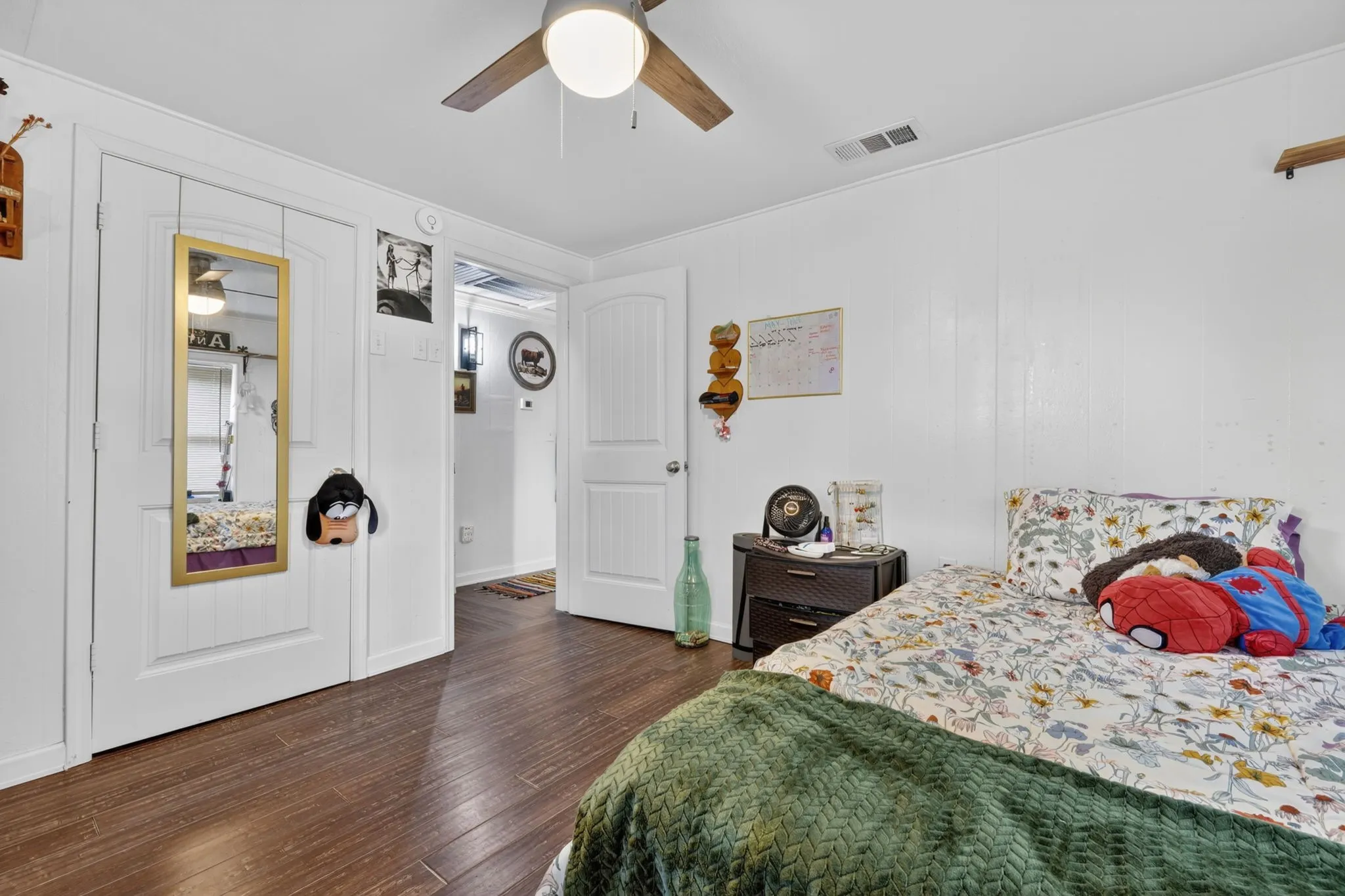 Bedroom featuring rich wood-finish flooring, white paneled walls, and a ceiling fan with integrated lighting