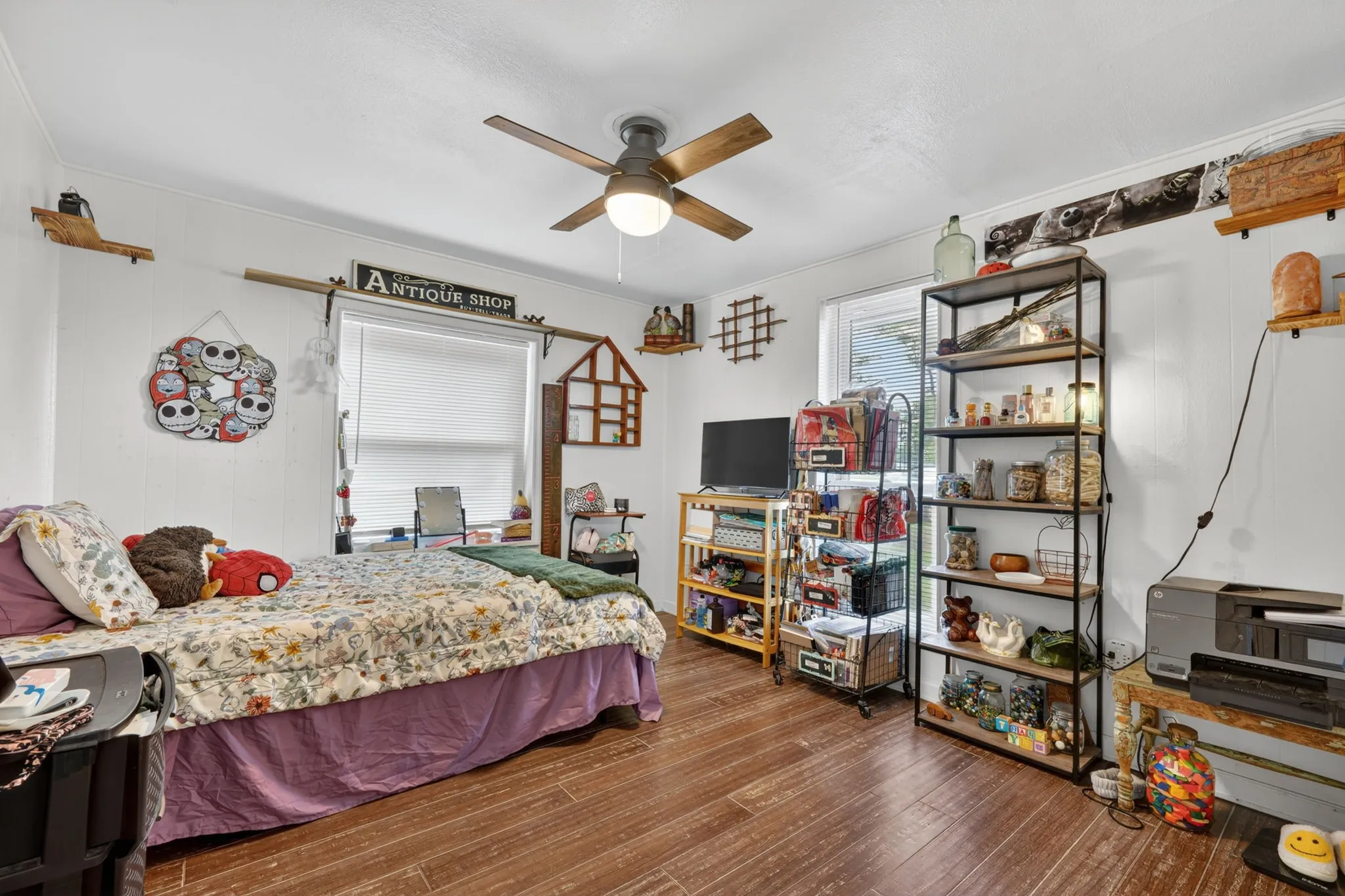 Bedroom featuring wood-finish flooring, a ceiling fan with integrated lighting, and a single window with blinds