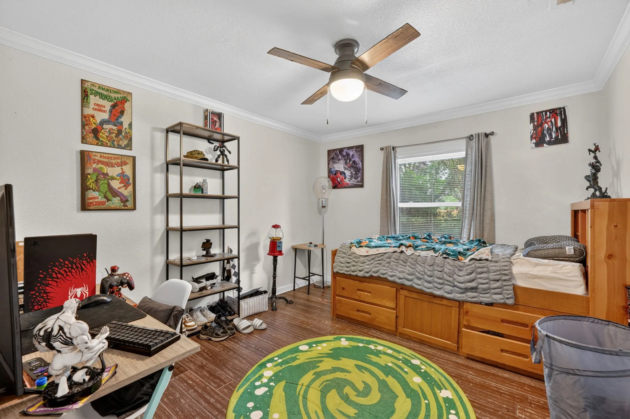 Wood-finish flooring throughout, featuring a ceiling fan with integrated lighting, a window with curtains, and crown molding
