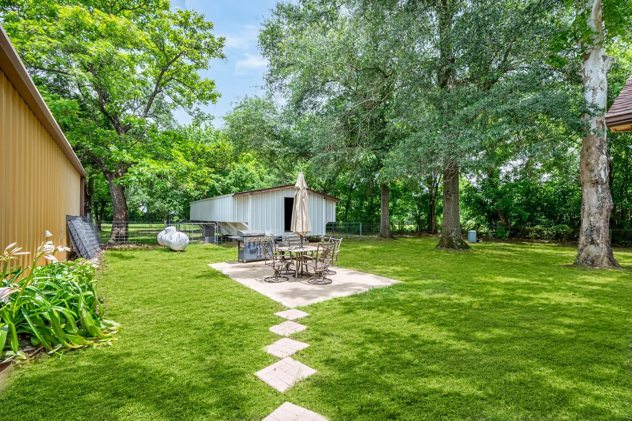 Expansive green lawn featuring mature trees, a rectangular concrete patio, and a paver stone walkway