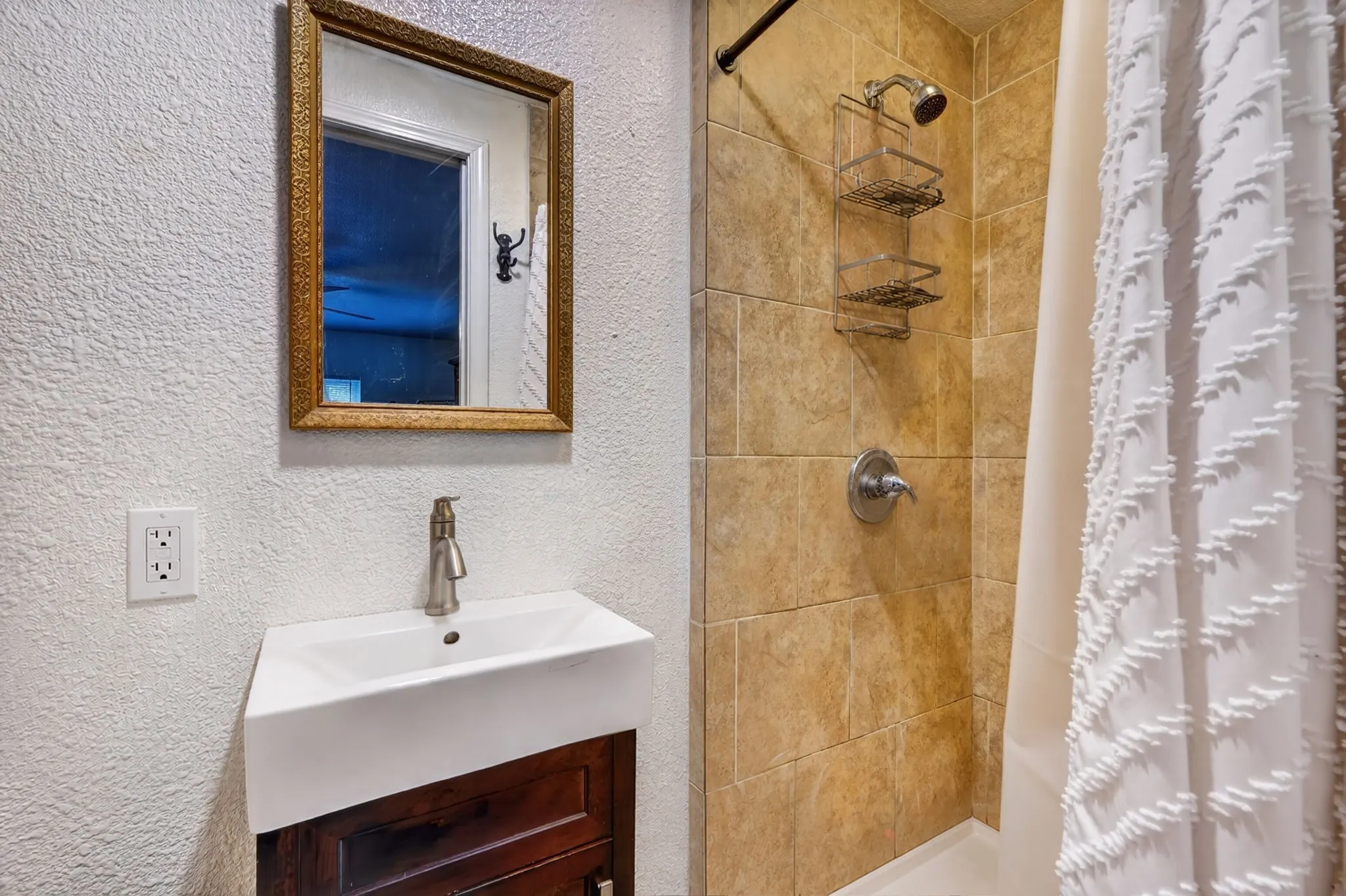 Bathroom featuring a wall-mounted vanity with a vessel sink, a framed mirror, and a shower with tiled walls and a built-in shower caddy