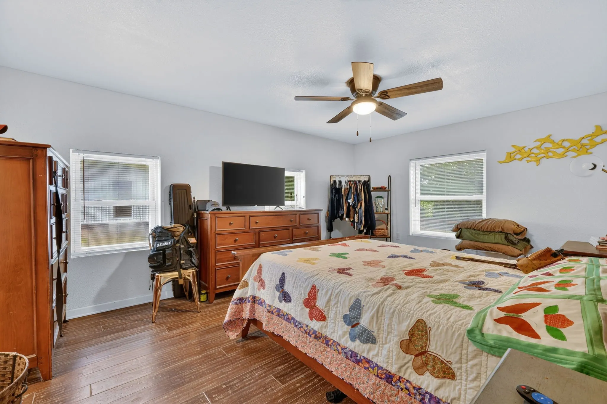Spacious room featuring wood-finish flooring, two windows, and a ceiling fan with integrated lighting