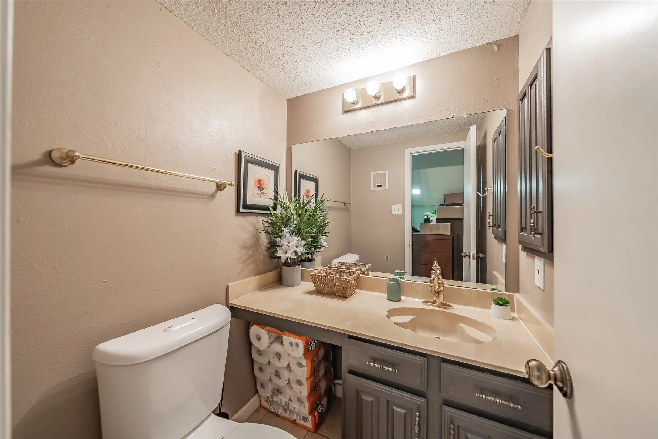 Bathroom vanity featuring a single basin sink set in a beige countertop, complemented by a large wall-mounted mirror and dark wood-finish cabinetry