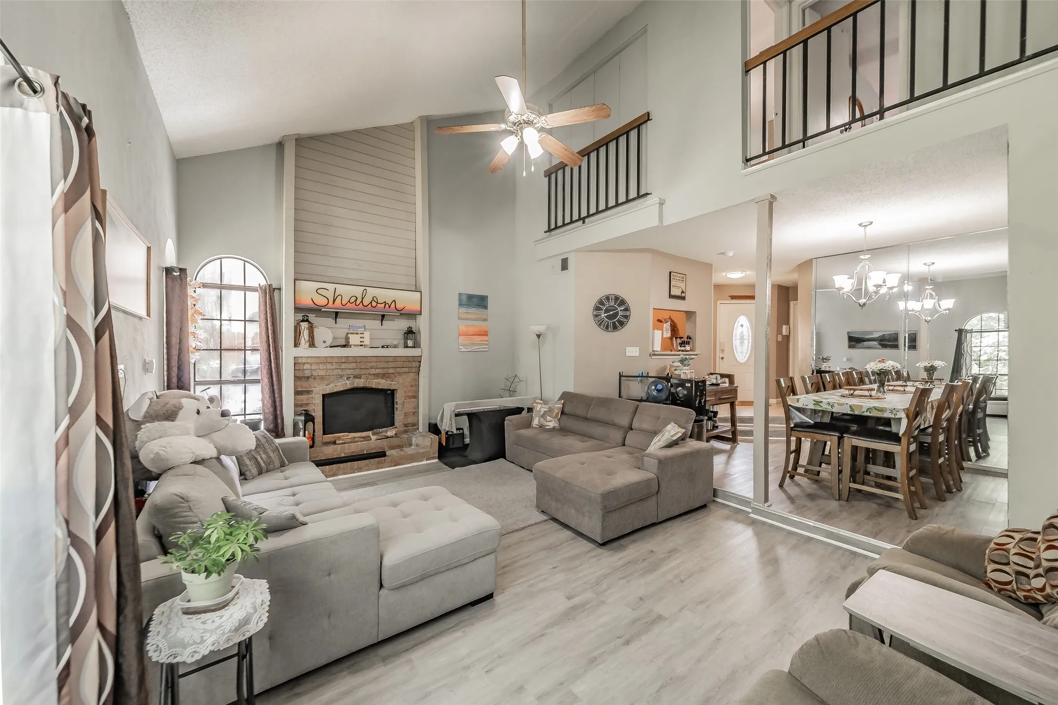 Vaulted living area featuring a brick fireplace with a shiplap accent wall, wood-finish flooring, a ceiling fan, and an arched window