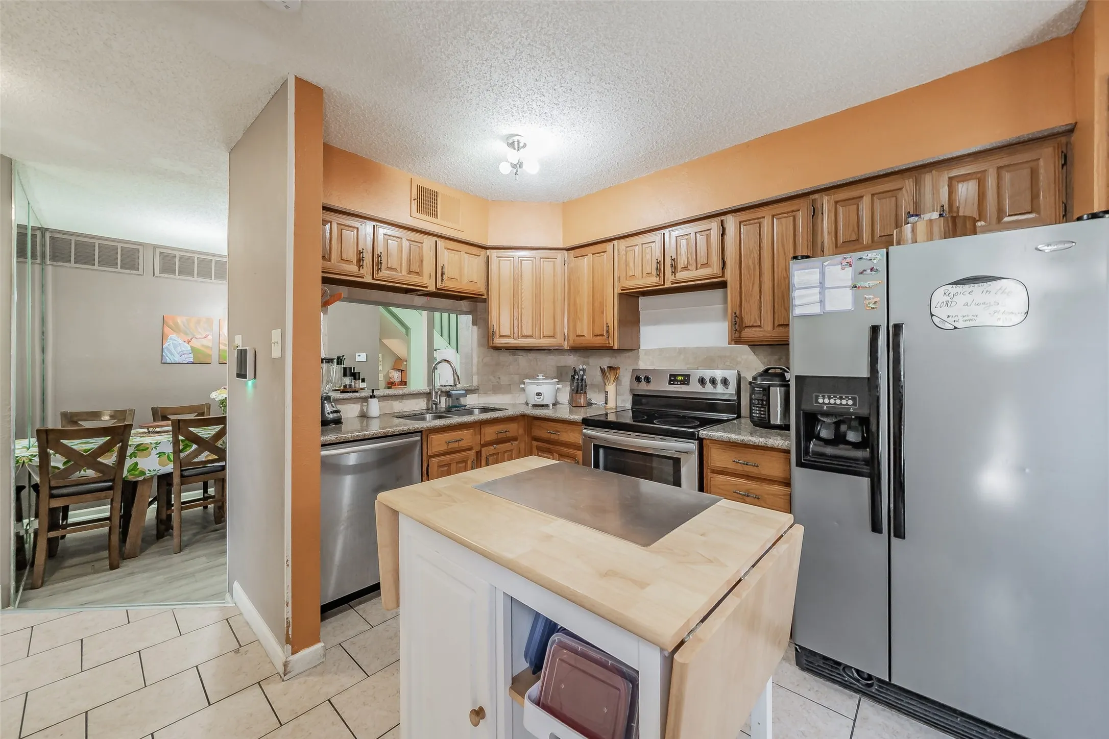 Kitchen featuring wood cabinetry, stainless steel appliances, granite-style countertops, and tile flooring