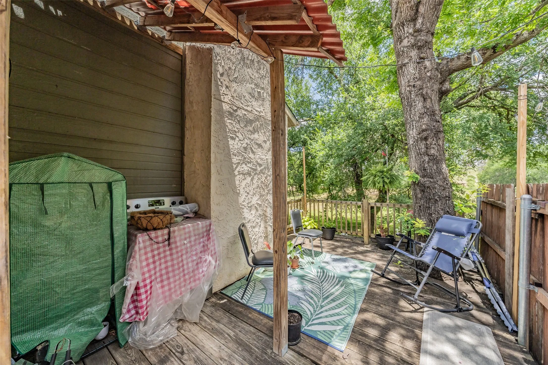 Wooden deck patio featuring a wood-slat privacy fence, stucco pillar, and mature tree canopy